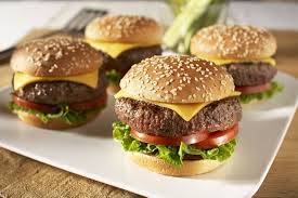 Four cheeseburgers with sesame seed buns, lettuce, tomato, and melted cheese on a white plate.