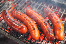 Four sausages grilling over charcoal with visible grill marks and smoke.