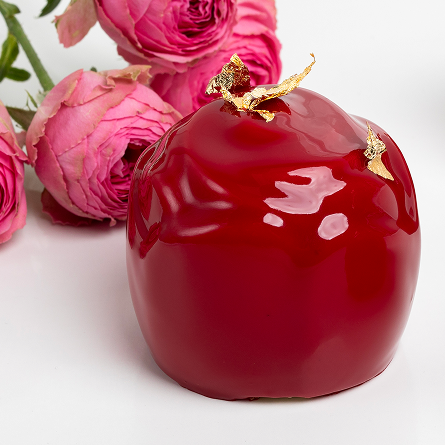 Czerwony deser monoporcja w kształcie jabłka z błyszczącą polewą i złotymi dekoracjami, obok leżą różowe róże.