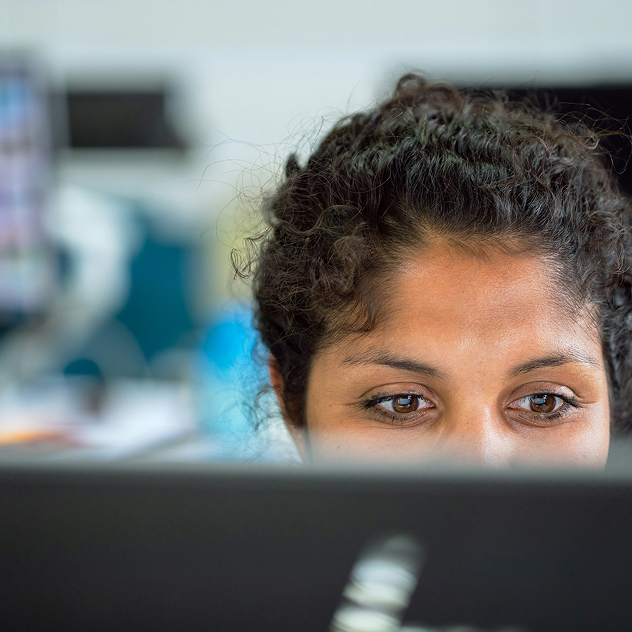 Close-up of a woman with curly hair focused on a computer screen in an office setting.