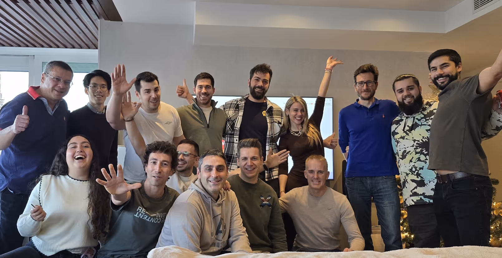Group photo of smiling diverse adults indoors with hands raised and thumbs up, suggesting celebration or camaraderie.
