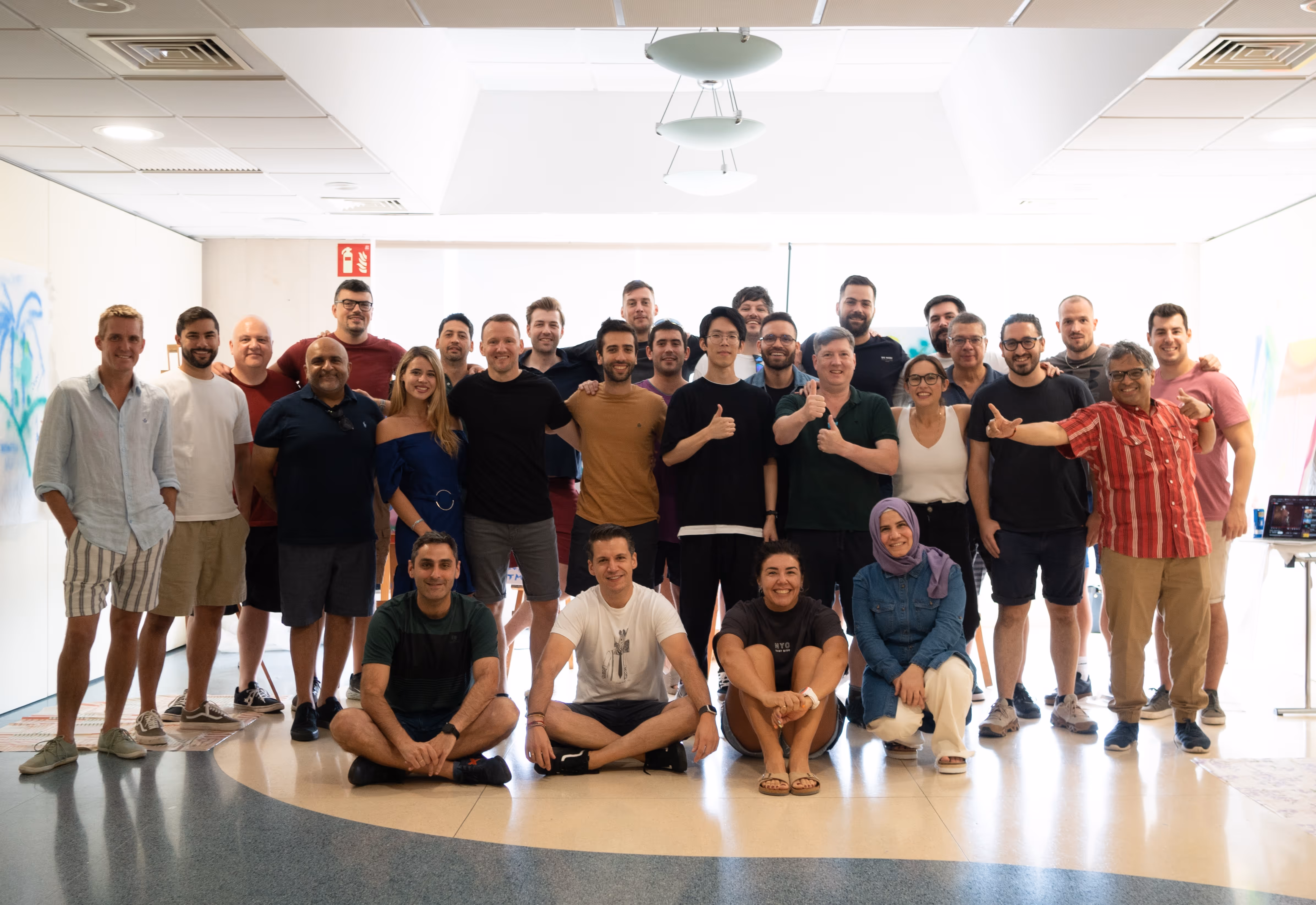 Large diverse group of men and women smiling and posing indoors in two rows, some standing and some sitting on the floor.