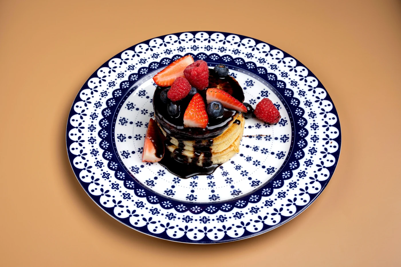 Pancakes ułożone w stos, z ciemną polewą i świeżymi owocami.