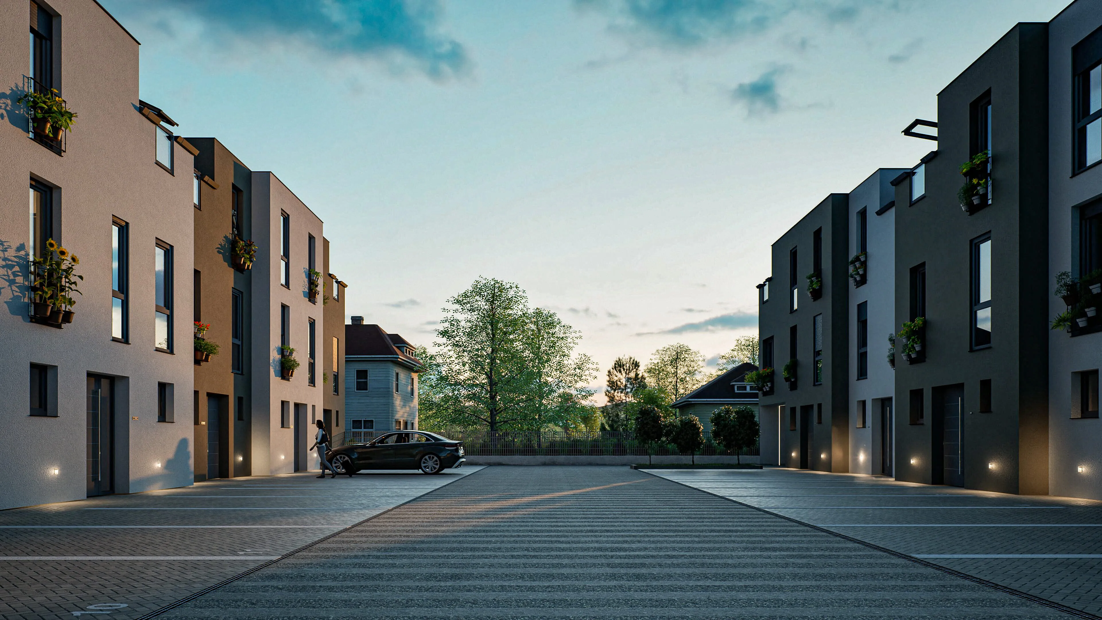 Parkplatz zwischen modernen Wohngebäuden bei Sonnenuntergang, links eine Person neben einem schwarzen Auto.