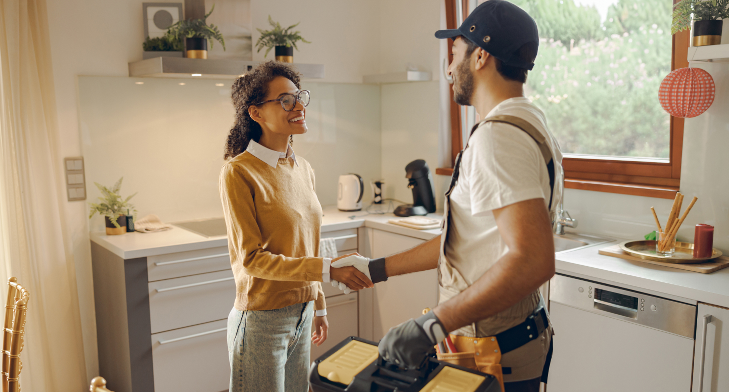 Woman shaking hands with a smiling maintenance vendor in a kitchen holding a toolbox.