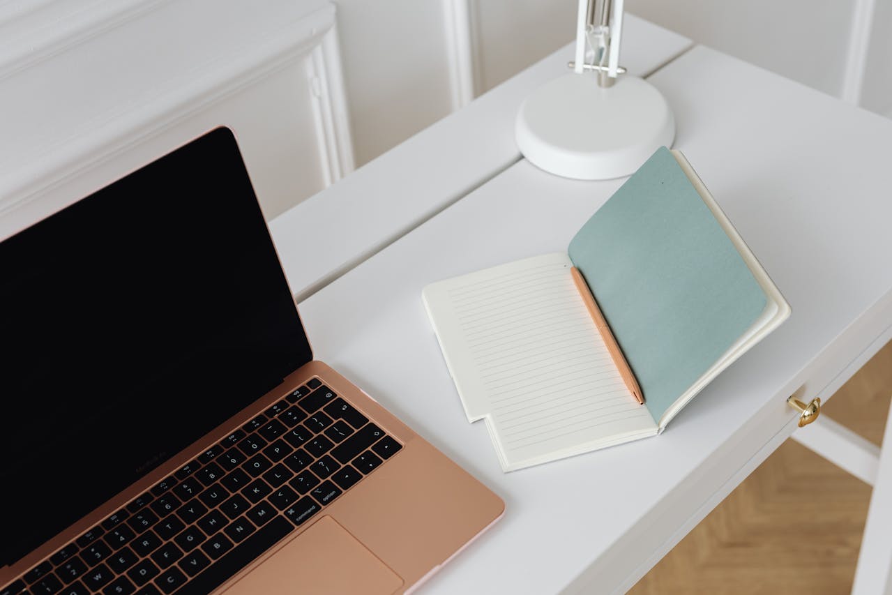 Note pad alongside a Macbook on a white table