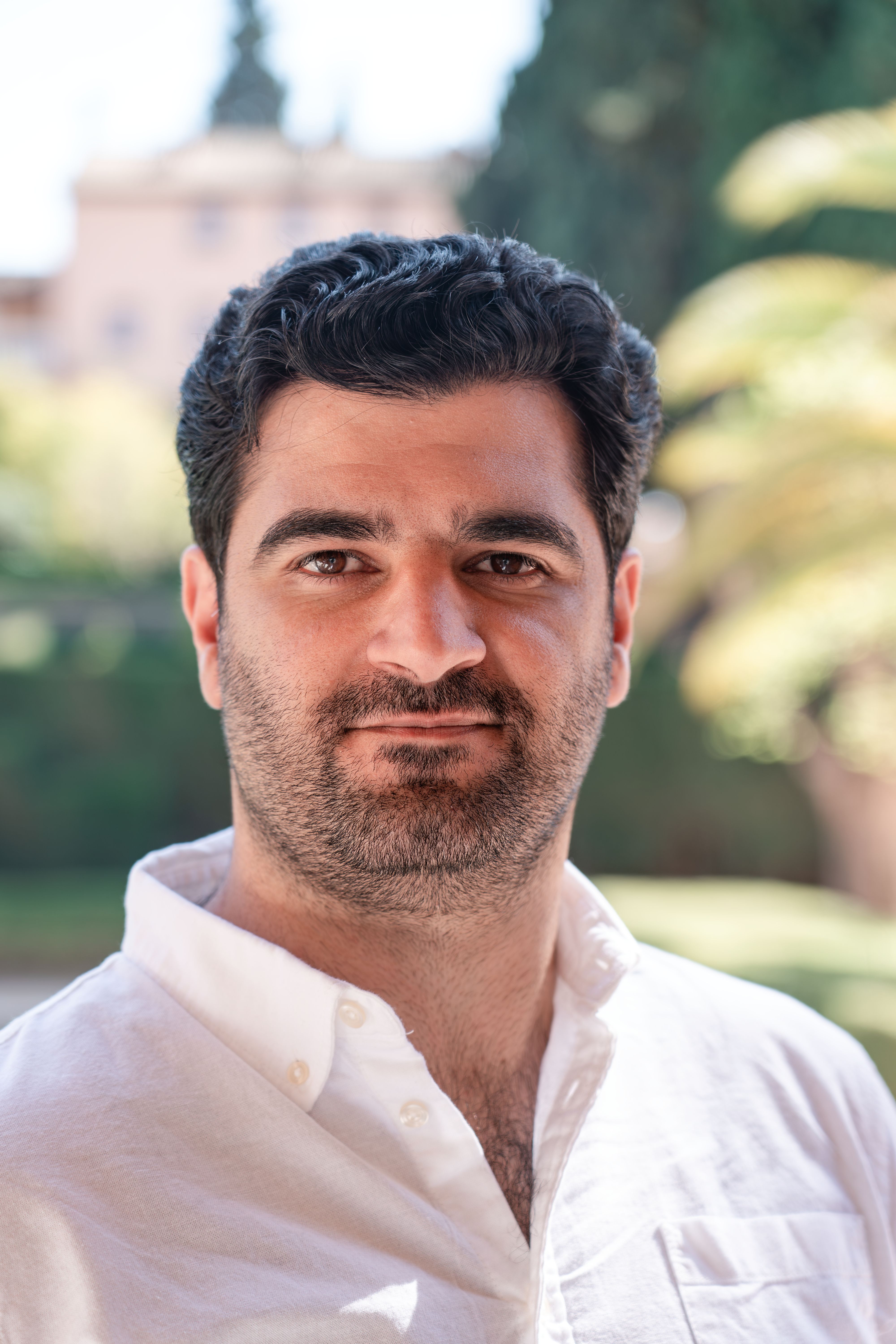 Smiling man with dark hair wearing a black leather jacket and black shirt against a black background.