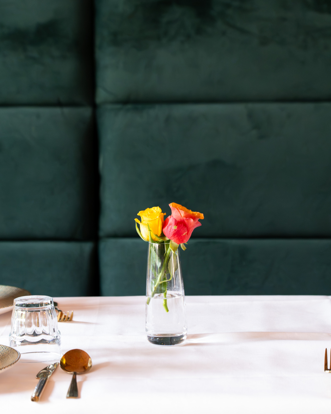 Table detail at Le Mont Liban — roses in a glass vase on white linen against green velvet