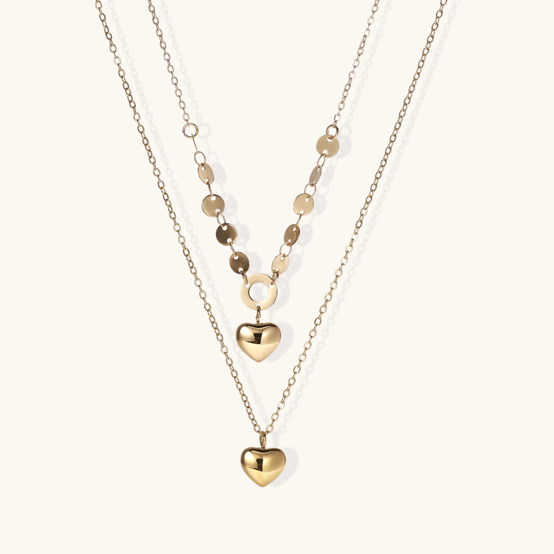 Three-layer 14K gold plated necklace with coin discs and dual heart pendants on cream background