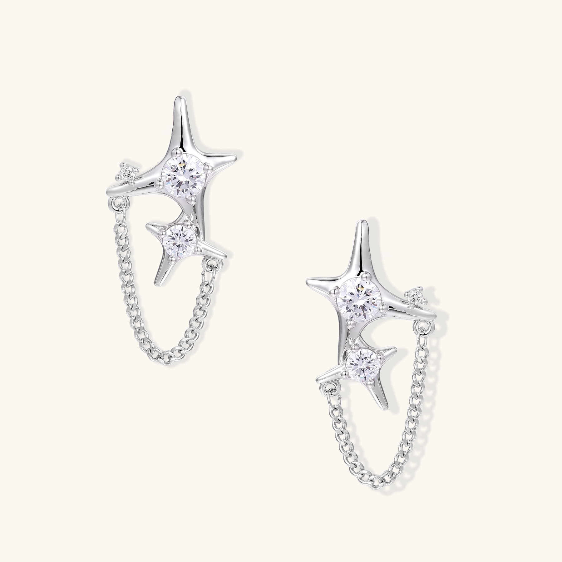 Silver star studs with crescent moon cutouts and zirconia stones connected by delicate chains on white background