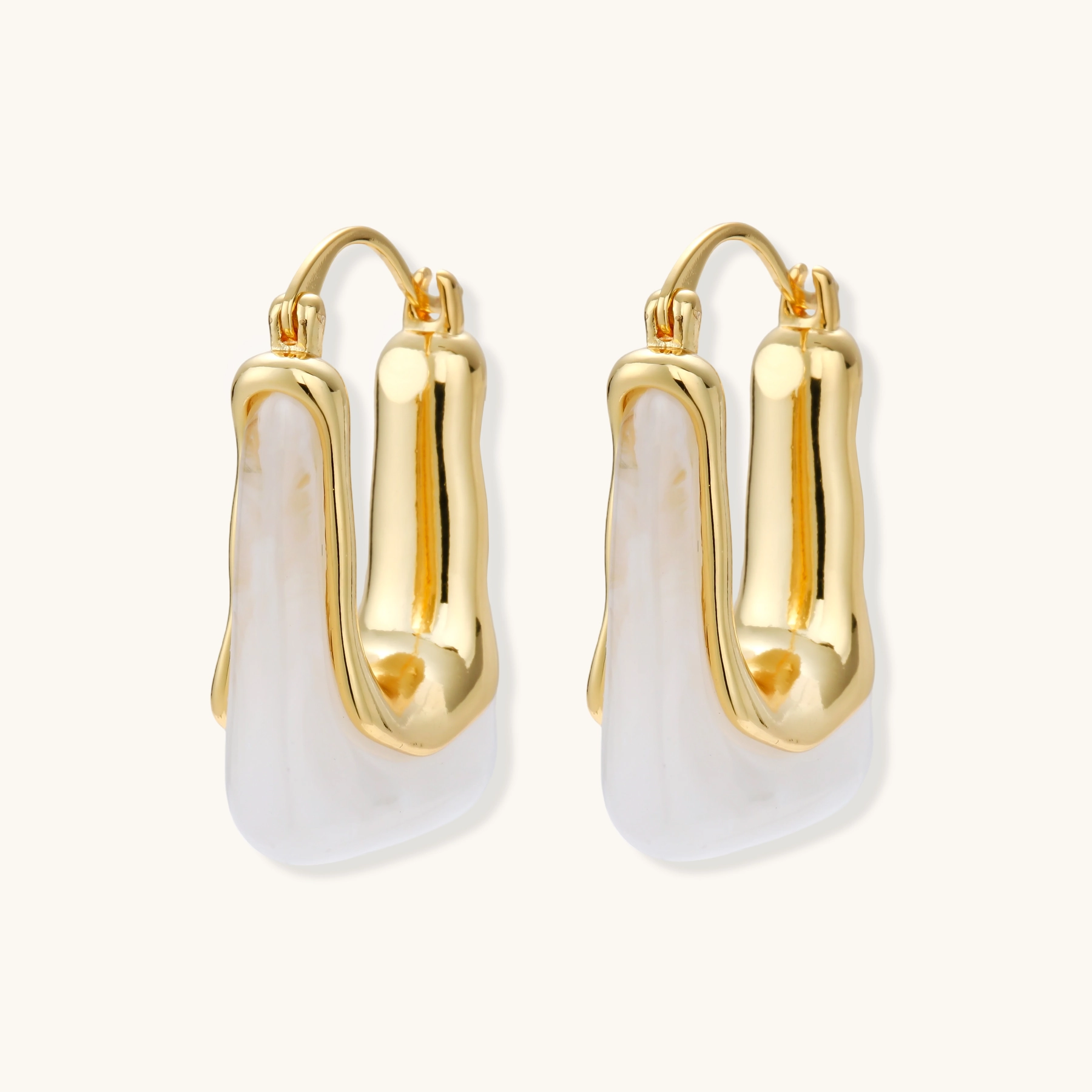 Sculptural gold-plated hoop earrings with flowing curved design and lever-back closure on cream background.