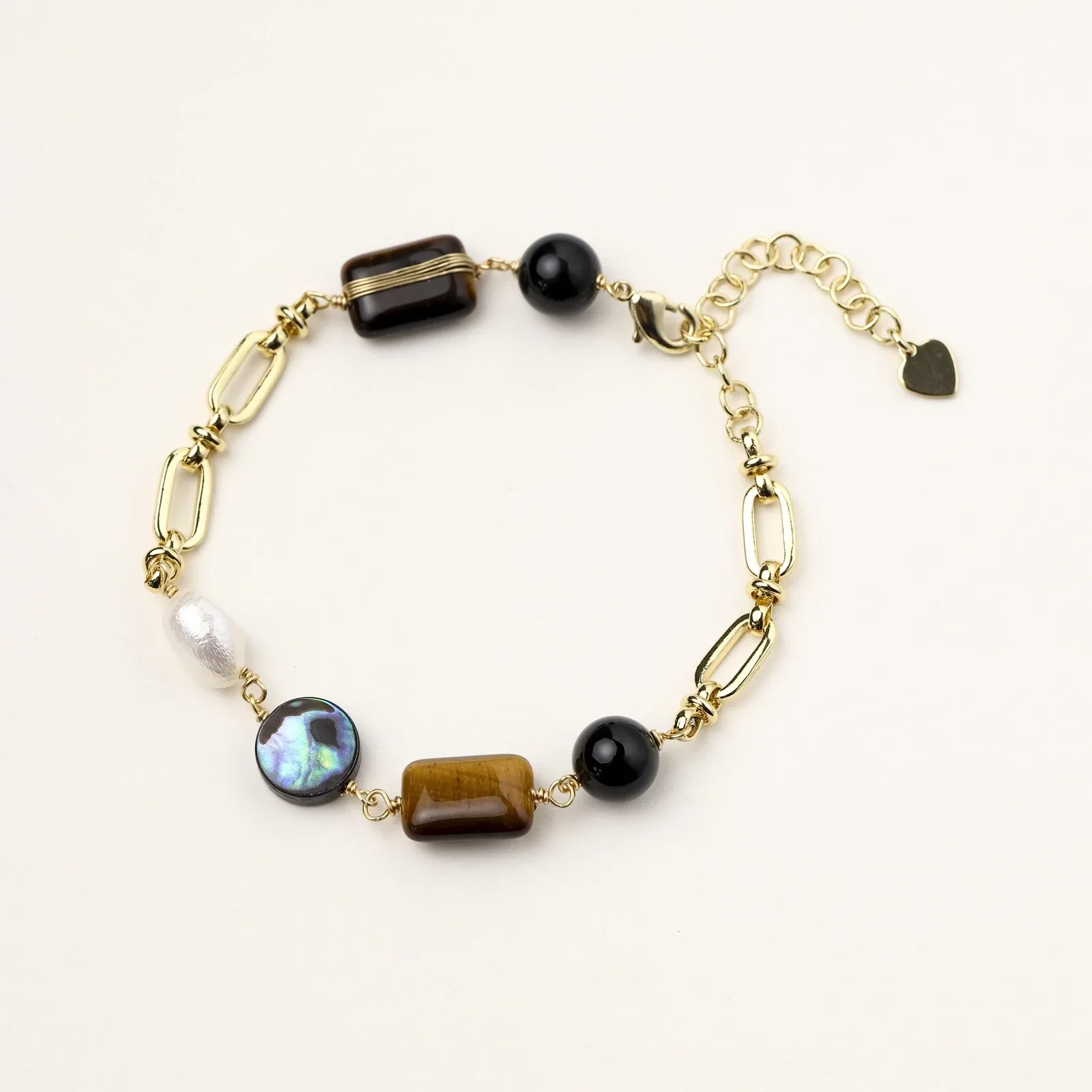 Gold chain bracelet with tiger's eye, obsidian, pearl, and iridescent abalone stones on cream background.