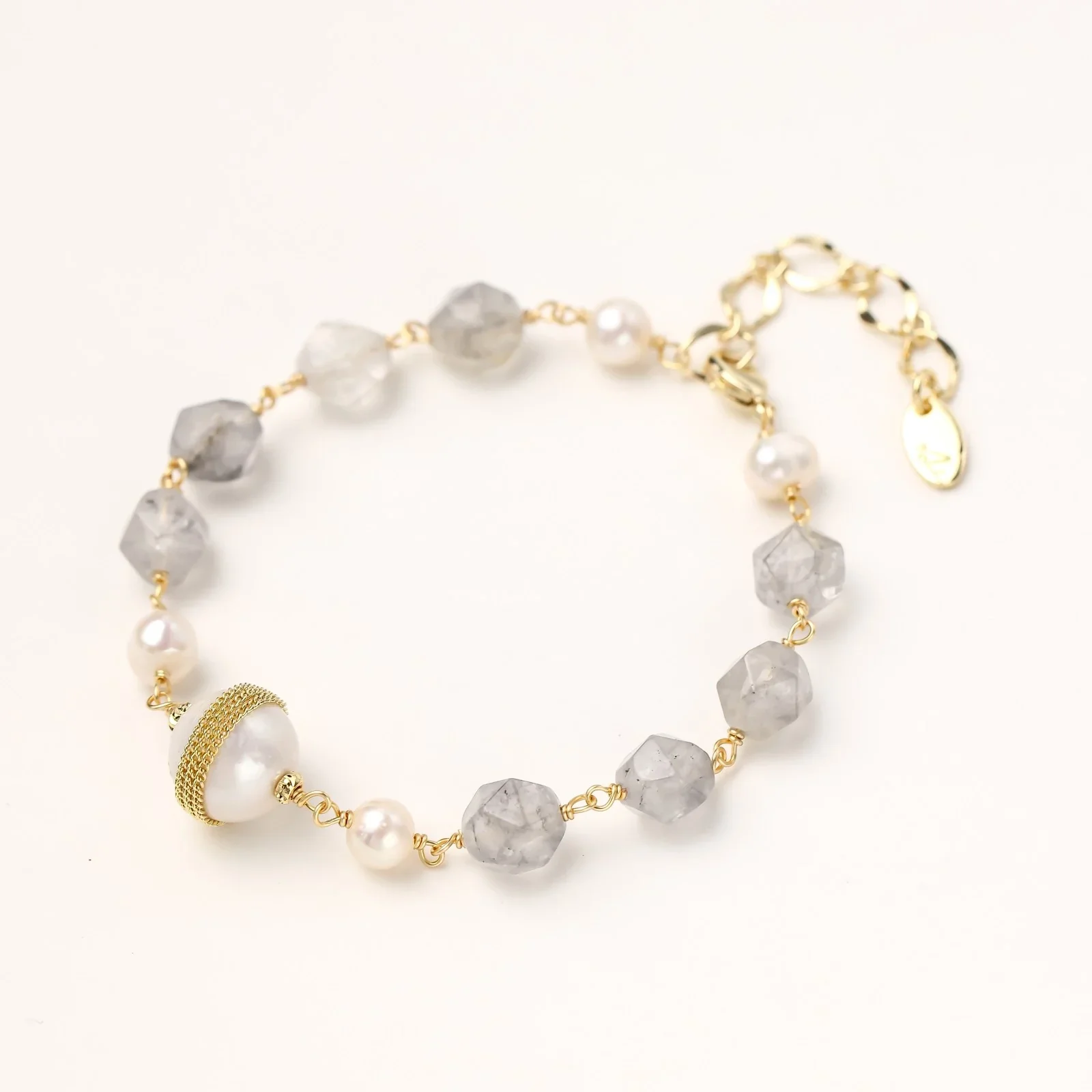 Bracelet with cloudy quartz beads, freshwater pearls, and gold-wrapped baroque pearl centerpiece on white background.