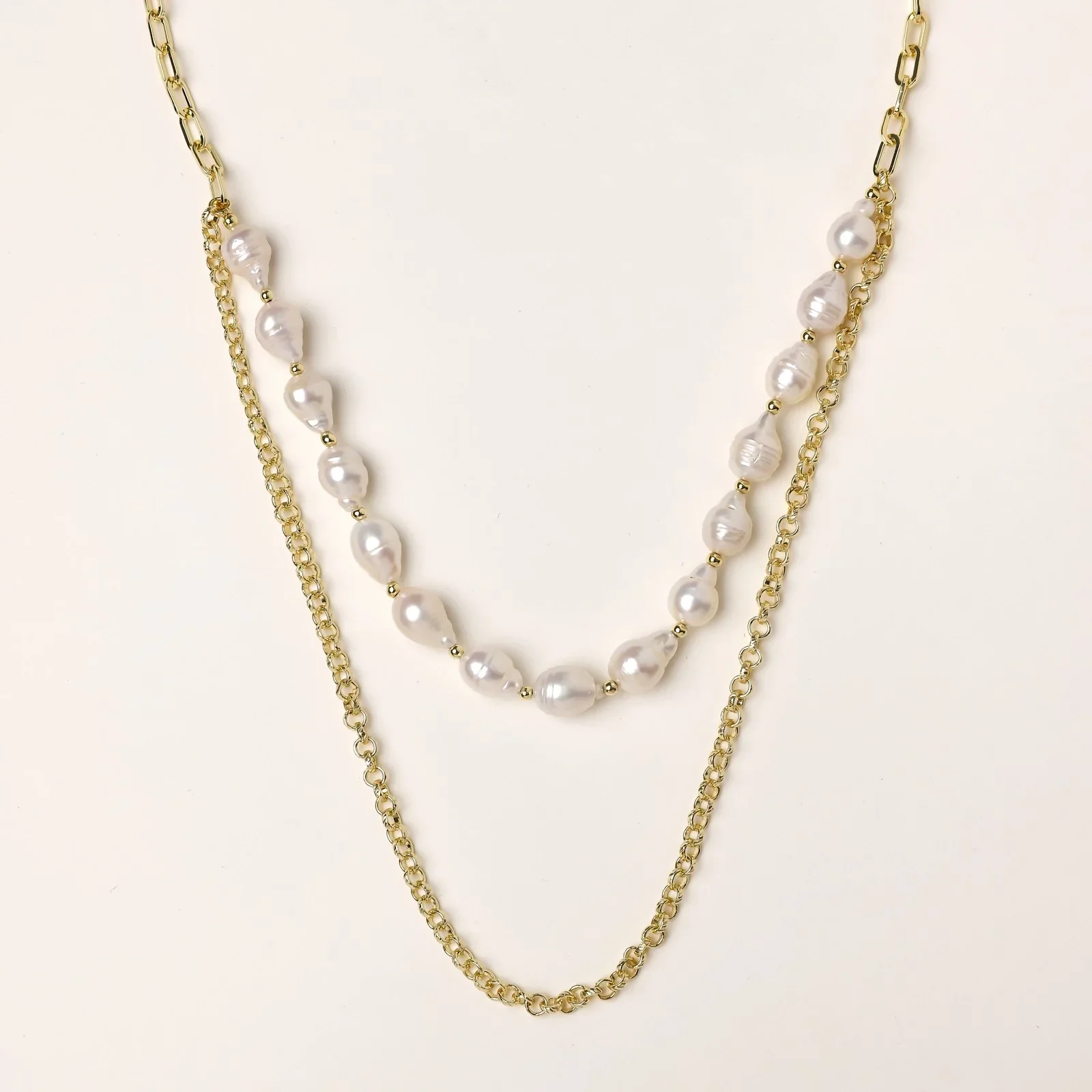 Layered gold chain necklace with organic baroque freshwater pearls and adjustable length on cream background
