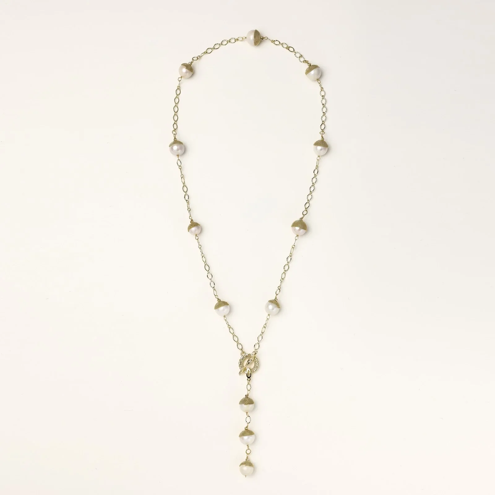 Gold-plated lariat necklace with baroque pearls and textured caps on cream background, showing adjustable Y-shaped design.