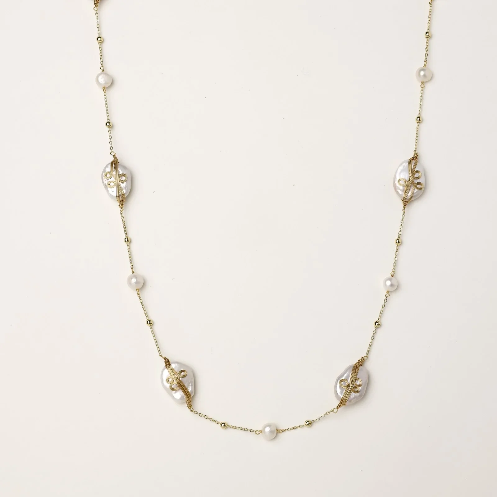 Long gold chain necklace with baroque pearls wrapped in leaf designs and small freshwater pearls spaced along the strand