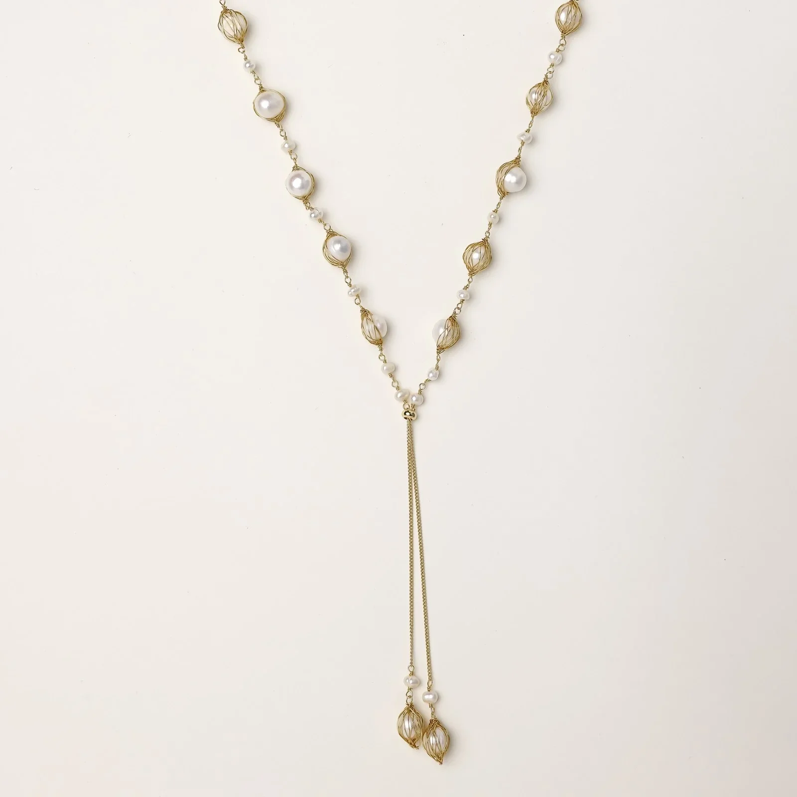 Adjustable gold lariat necklace with freshwater pearls nested in delicate cage settings and Y-shaped tassel drop