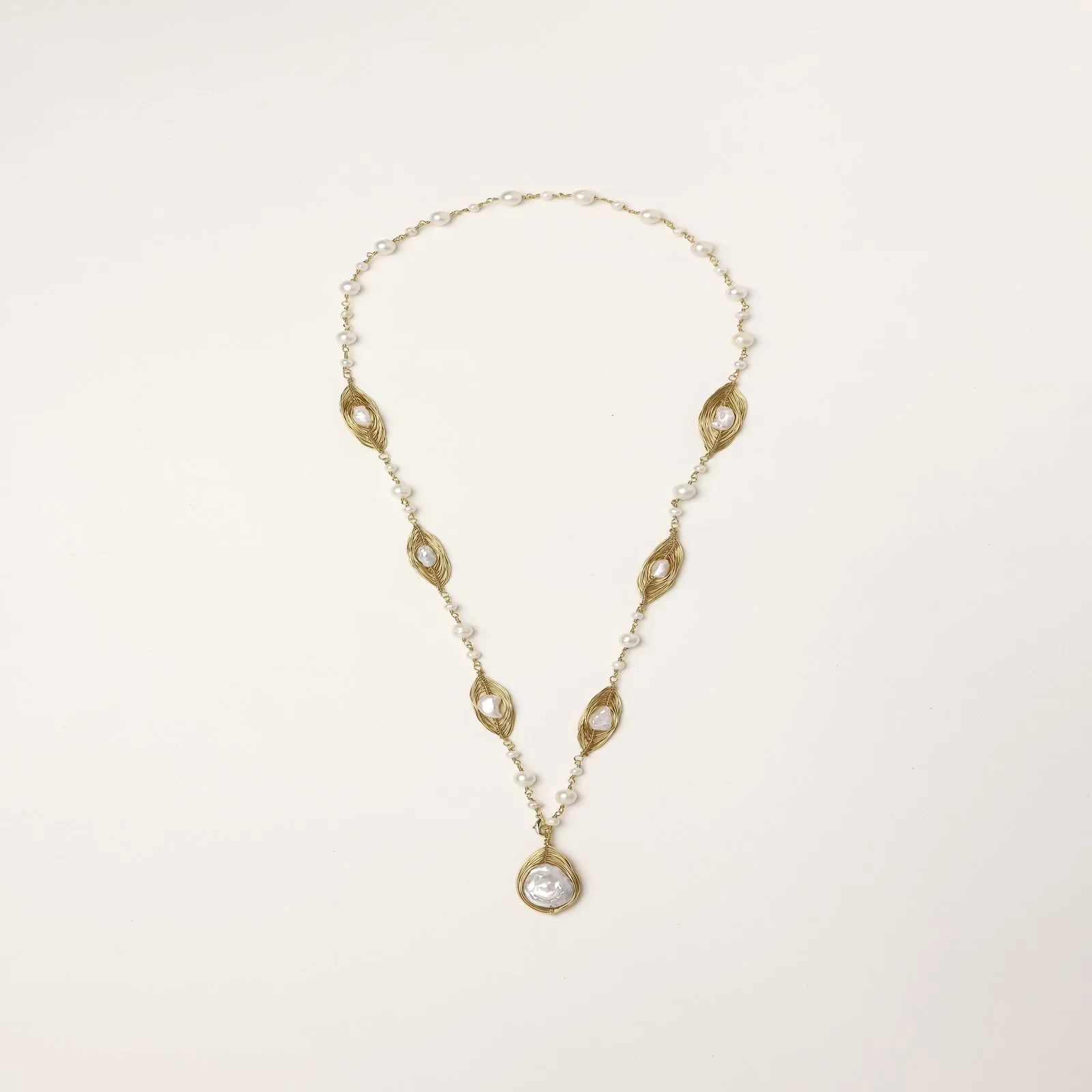 14K gold-plated necklace with eye-shaped stations and baroque pearl pendant on cream background