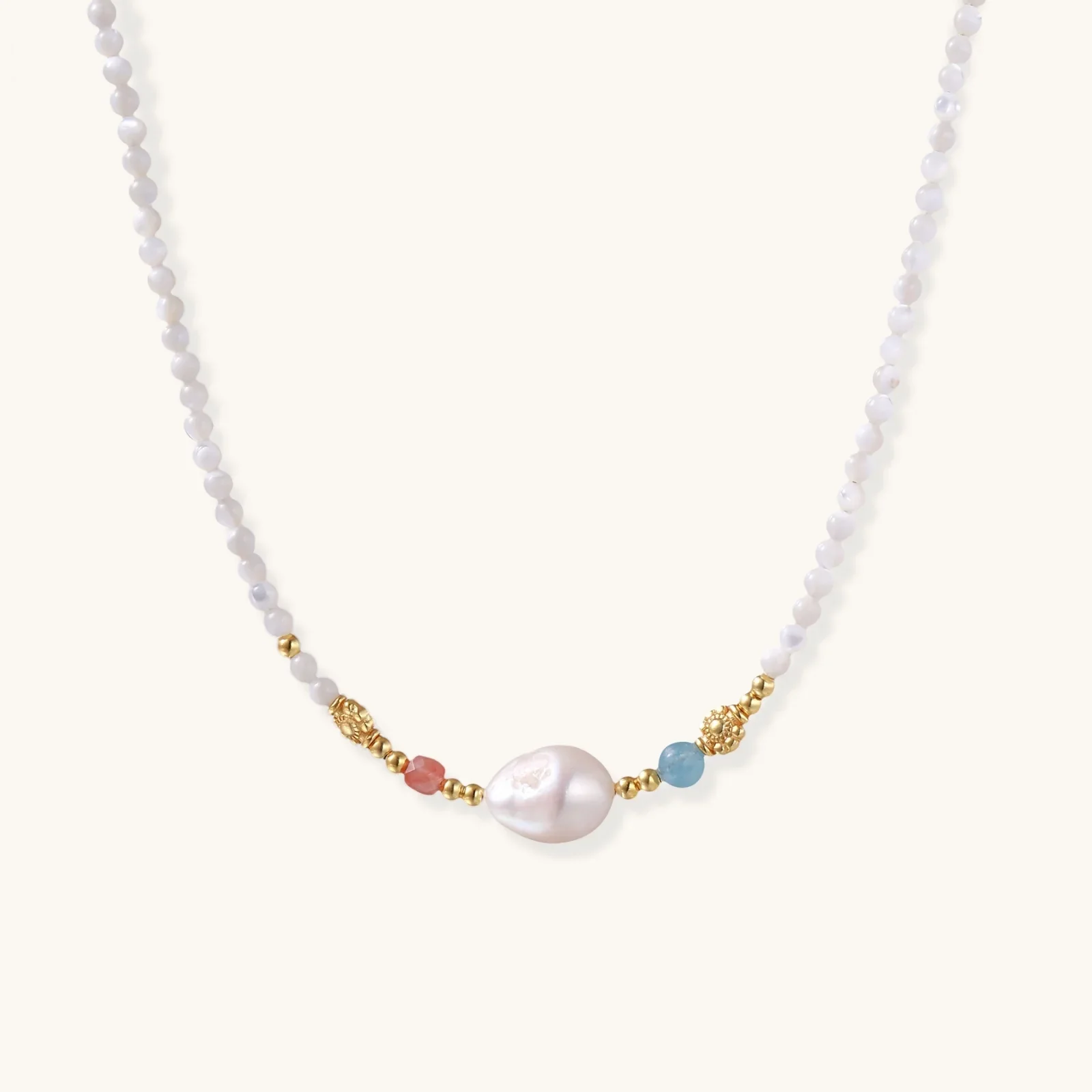Delicate white beaded necklace with baroque pearl center, gold accents, and coral and aqua gemstones on cream background.