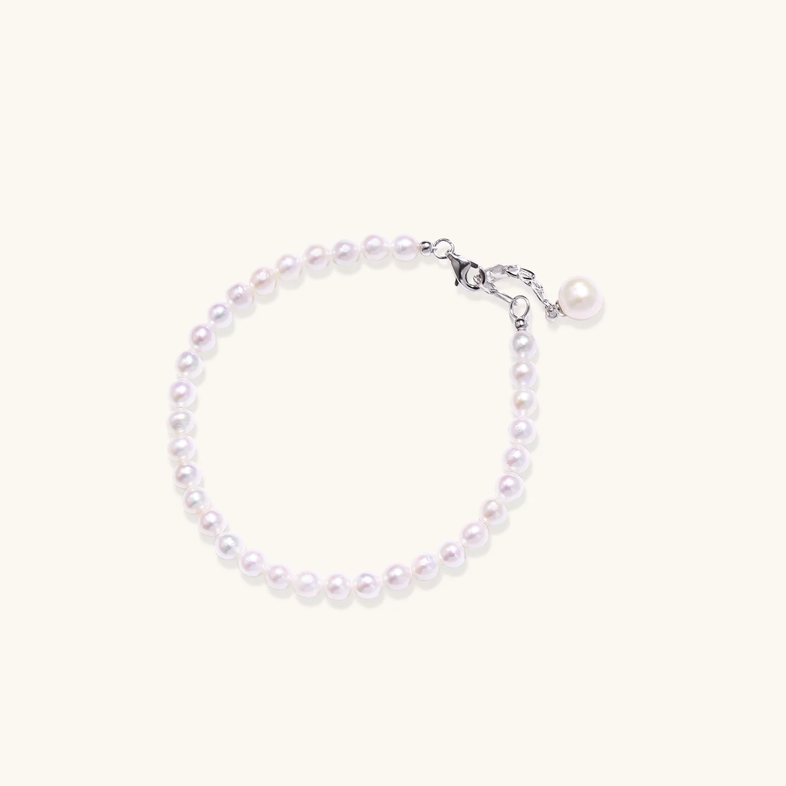 Delicate freshwater pearl bracelet with rhodium-plated silver clasp and single pearl drop charm on cream background