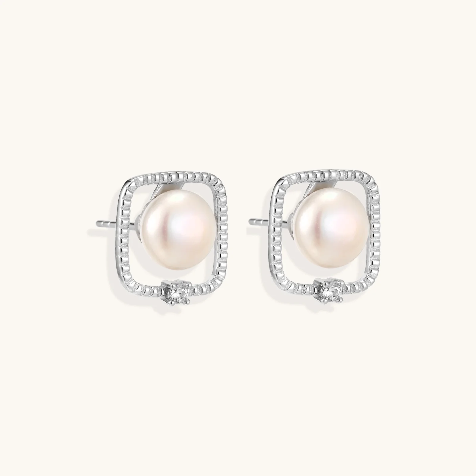 Rhodium-plated silver stud earrings with cushion frame, centered freshwater pearl, and tiny crystal accent