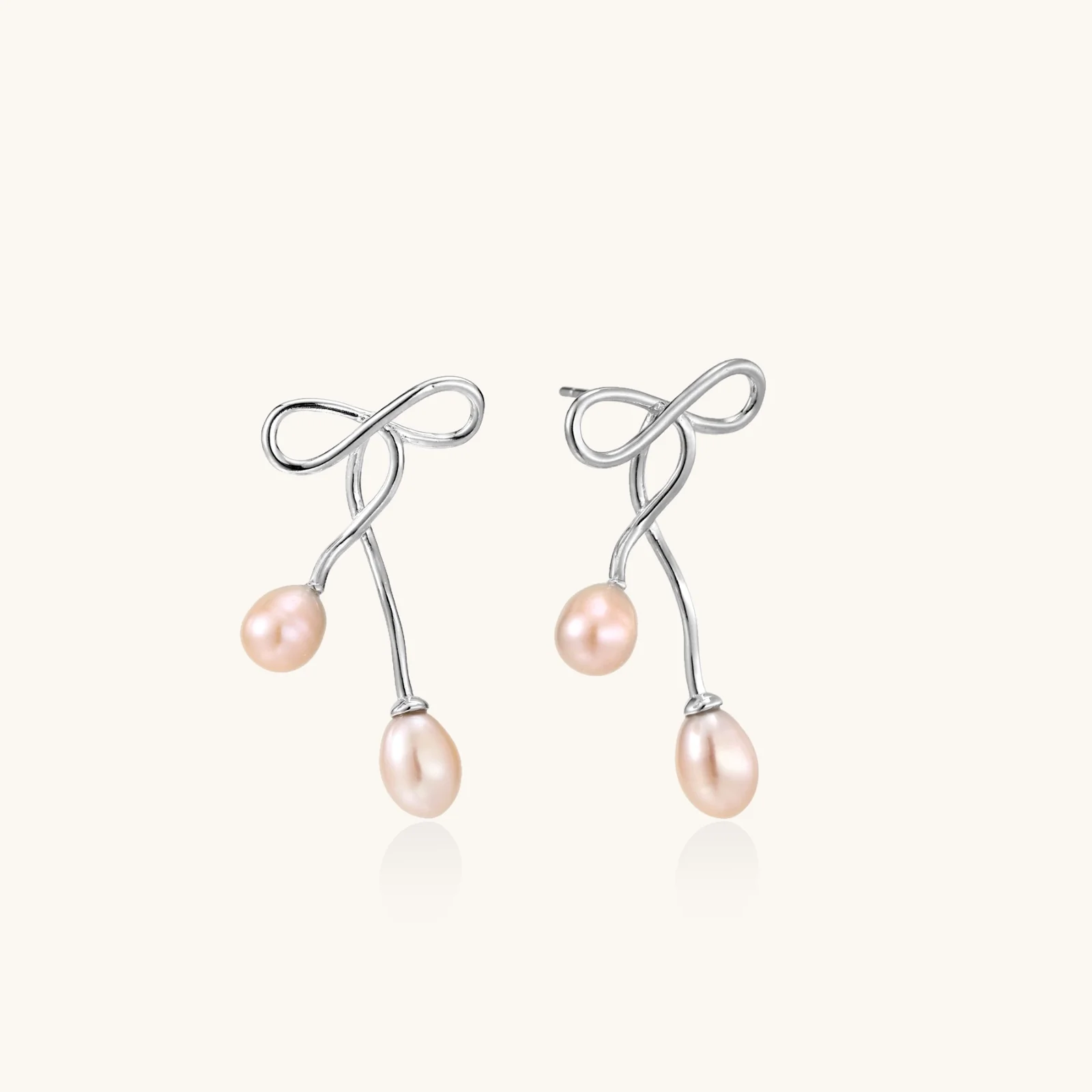 Rhodium-plated silver earrings with organic vine curves and two peachy freshwater pearls on cream background