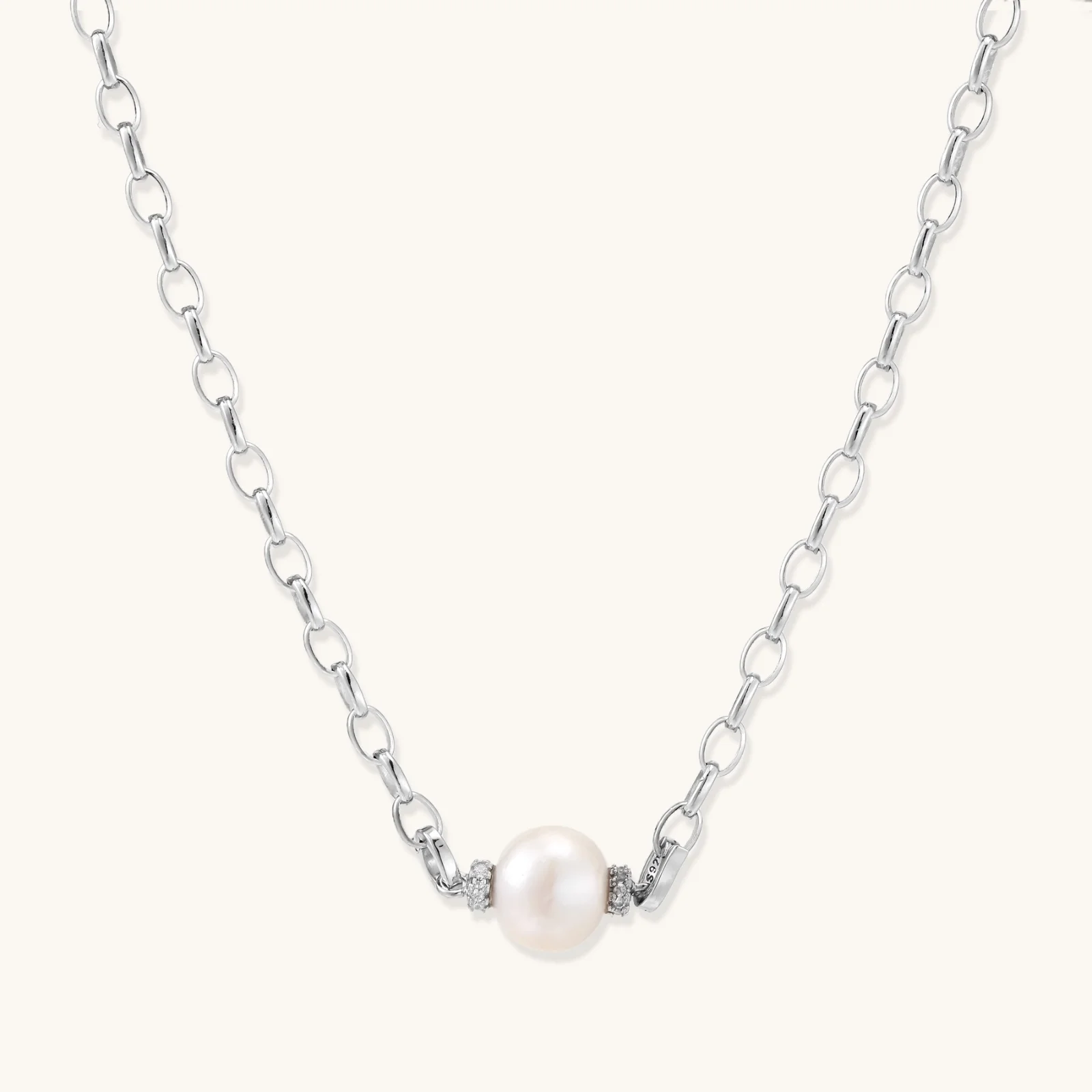 Dainty rhodium-plated silver chain necklace with centered 10mm freshwater pearl and crystal accents on cream background