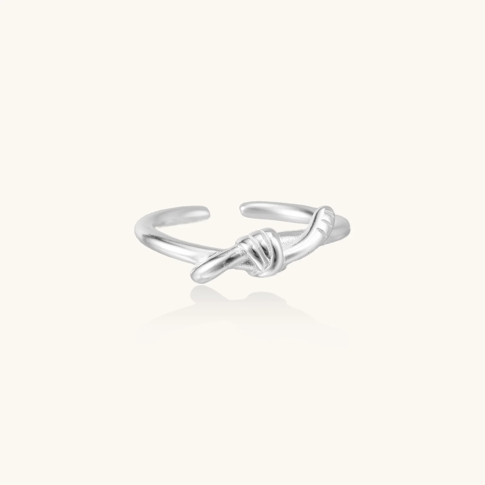 Delicate rhodium-plated silver ring with elegant knot design on cream background, adjustable band style