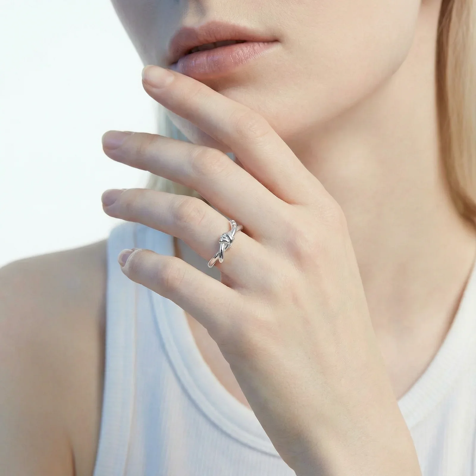 Delicate rhodium-plated silver ring with elegant knot design on cream background, adjustable band style