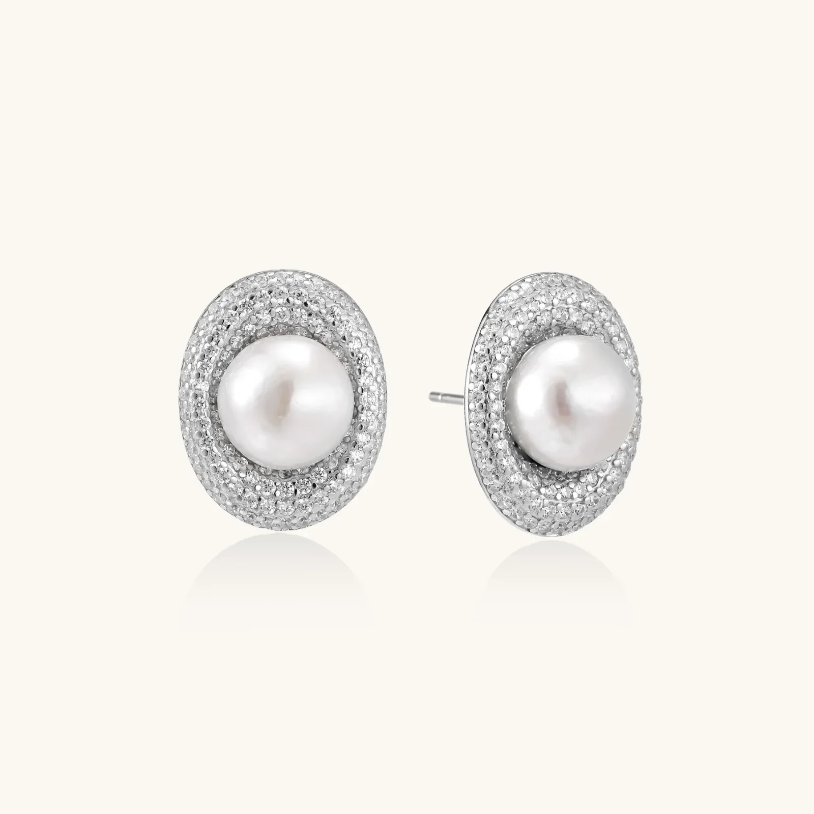 Oval rhodium-plated silver studs featuring freshwater pearls surrounded by pavé crystal halo on white background