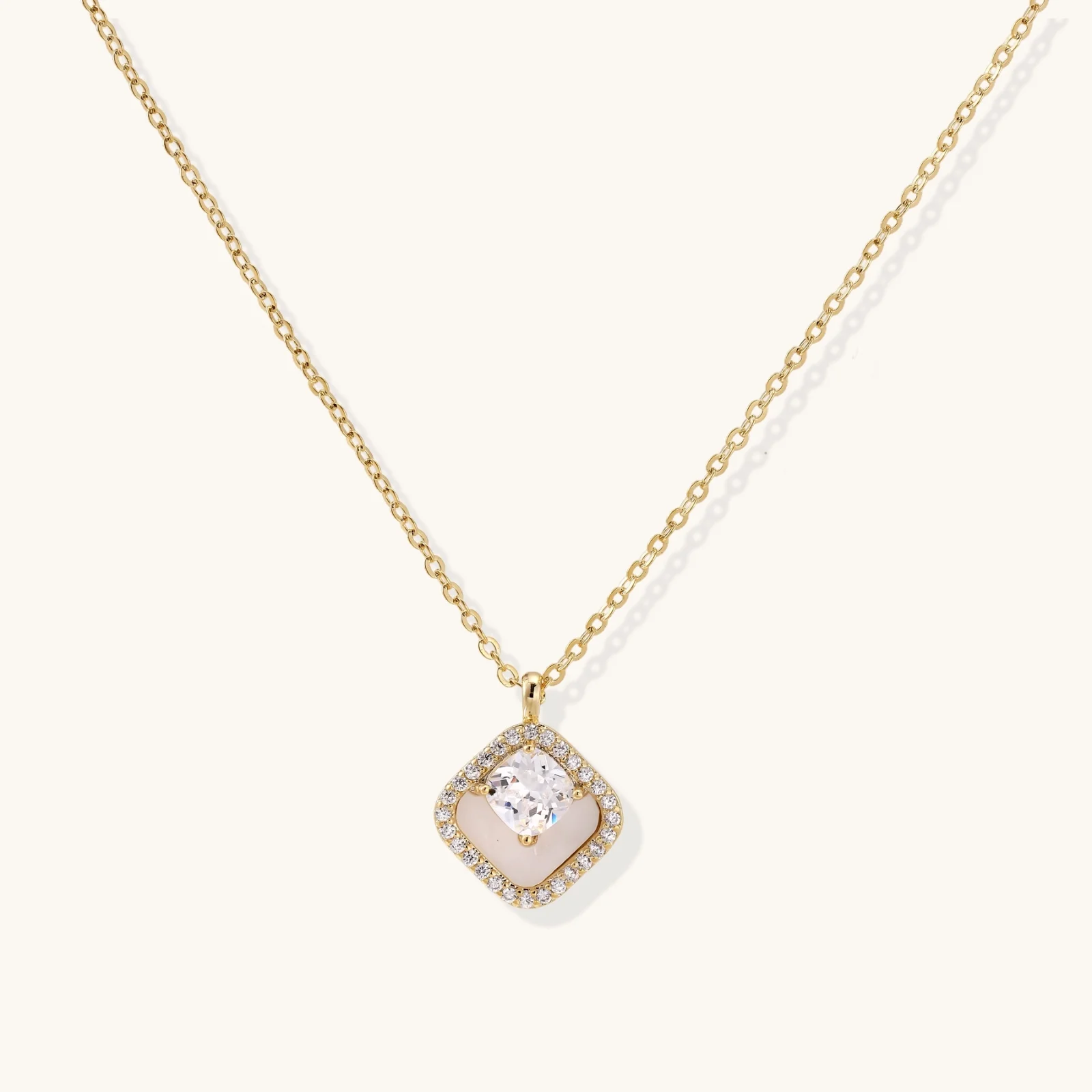 Gold quatrefoil pendant with crystal center on iridescent mother-of-pearl base, adjustable gold chain on cream background