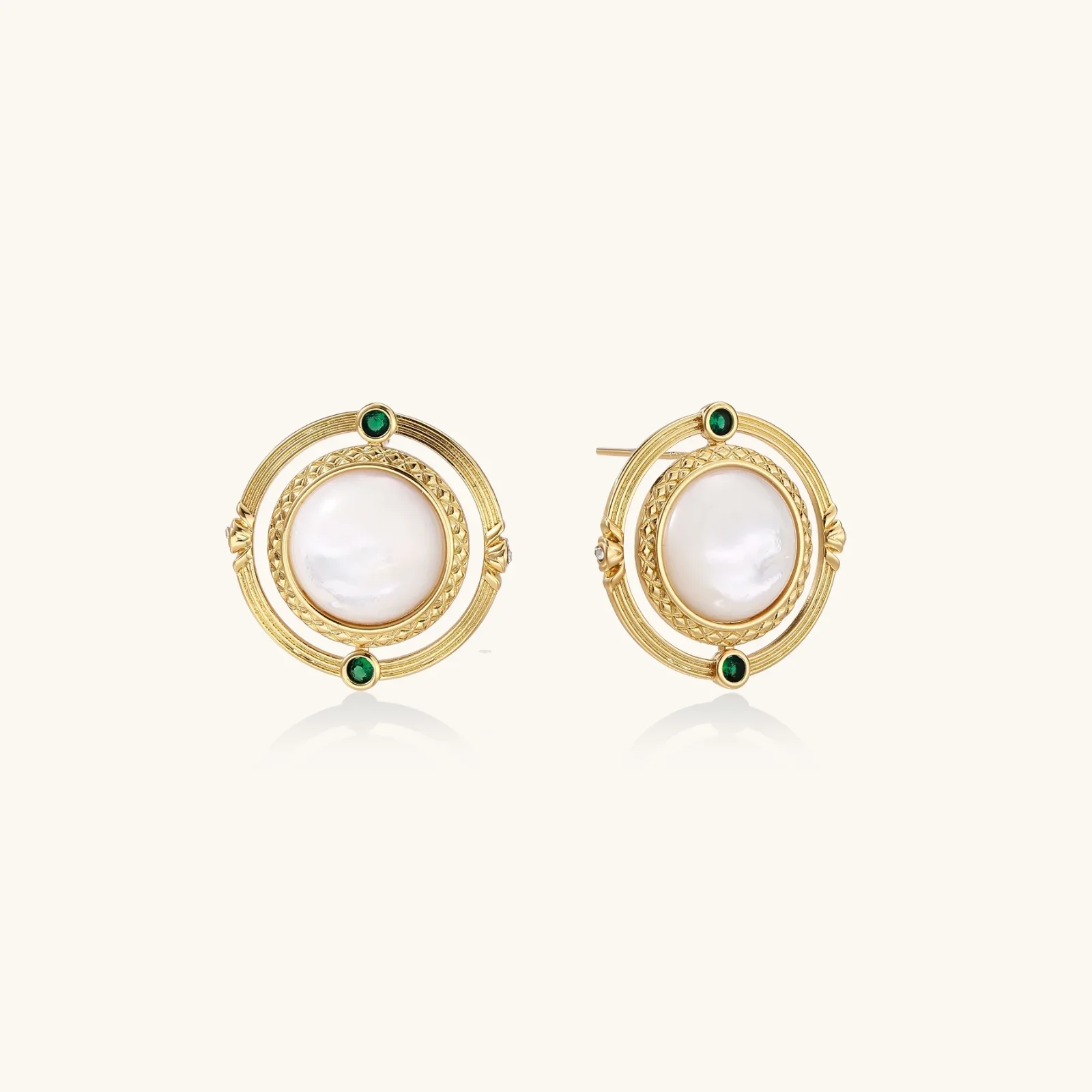 Circular gold stud earrings with iridescent mother-of-pearl center and green zirconia accents on cream background.