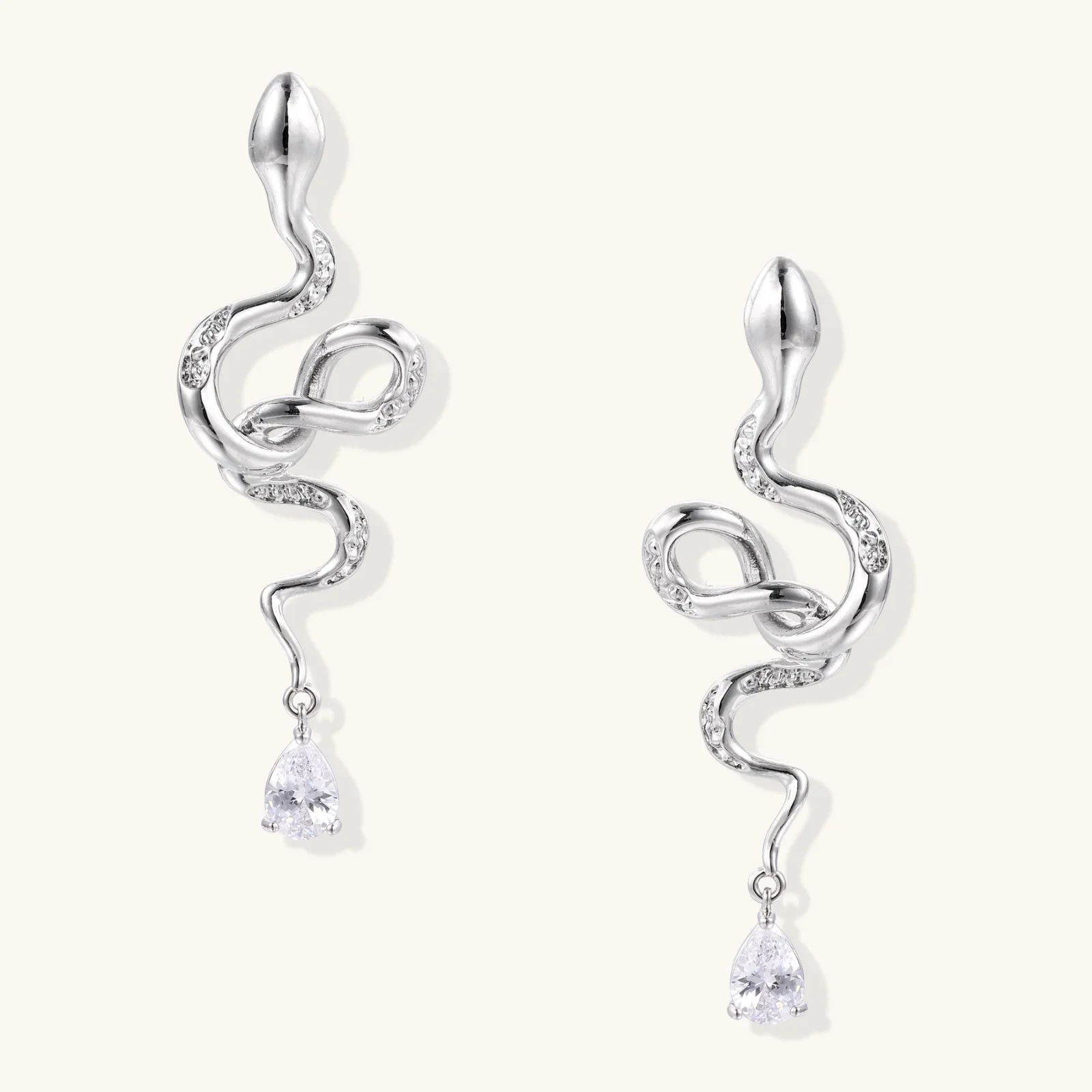 Silver snake-shaped drop earrings with crystal accents and teardrop stone dangles on cream background.