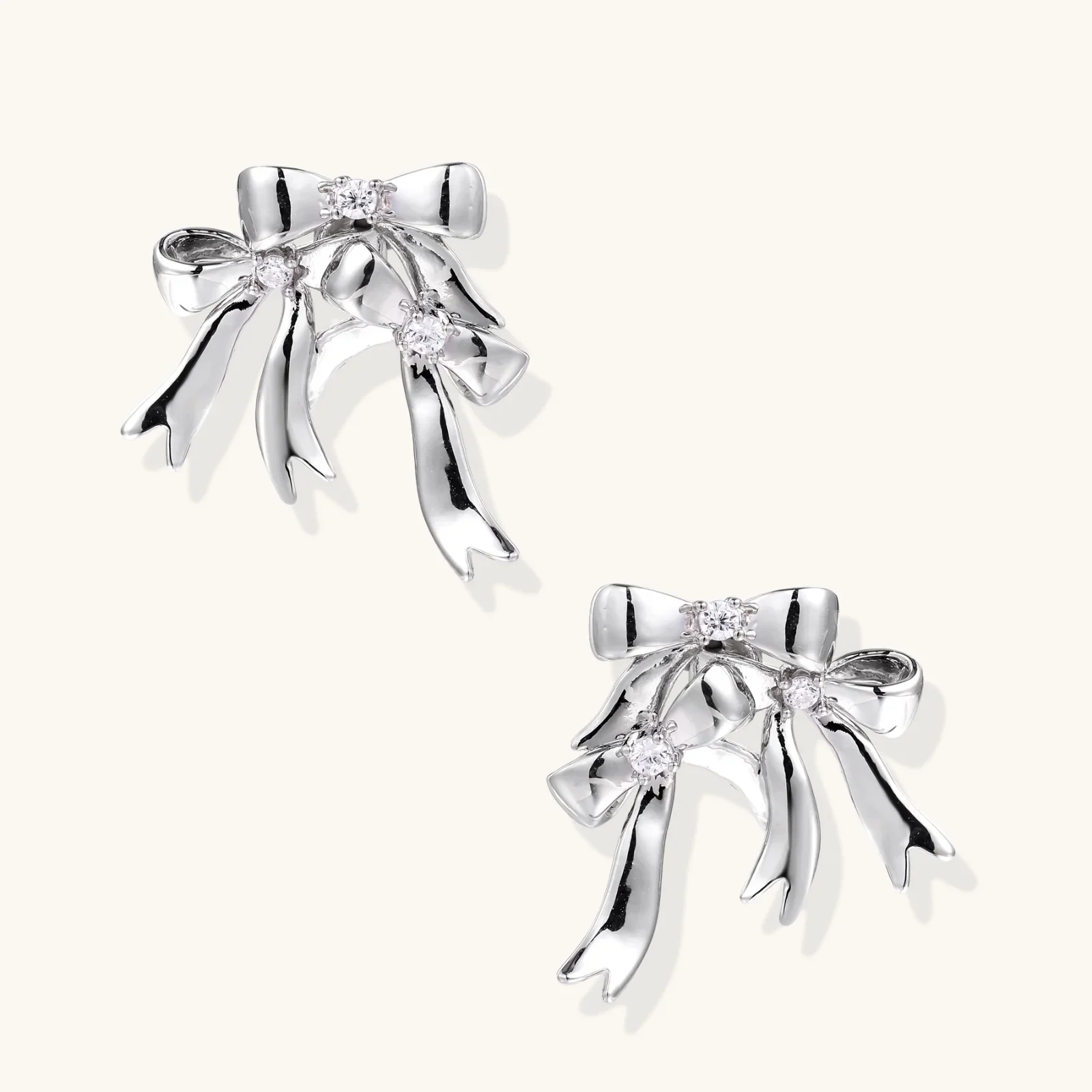 Sculptural bow earrings in polished white gold plate with sparkling zirconia stones and flowing ribbon details