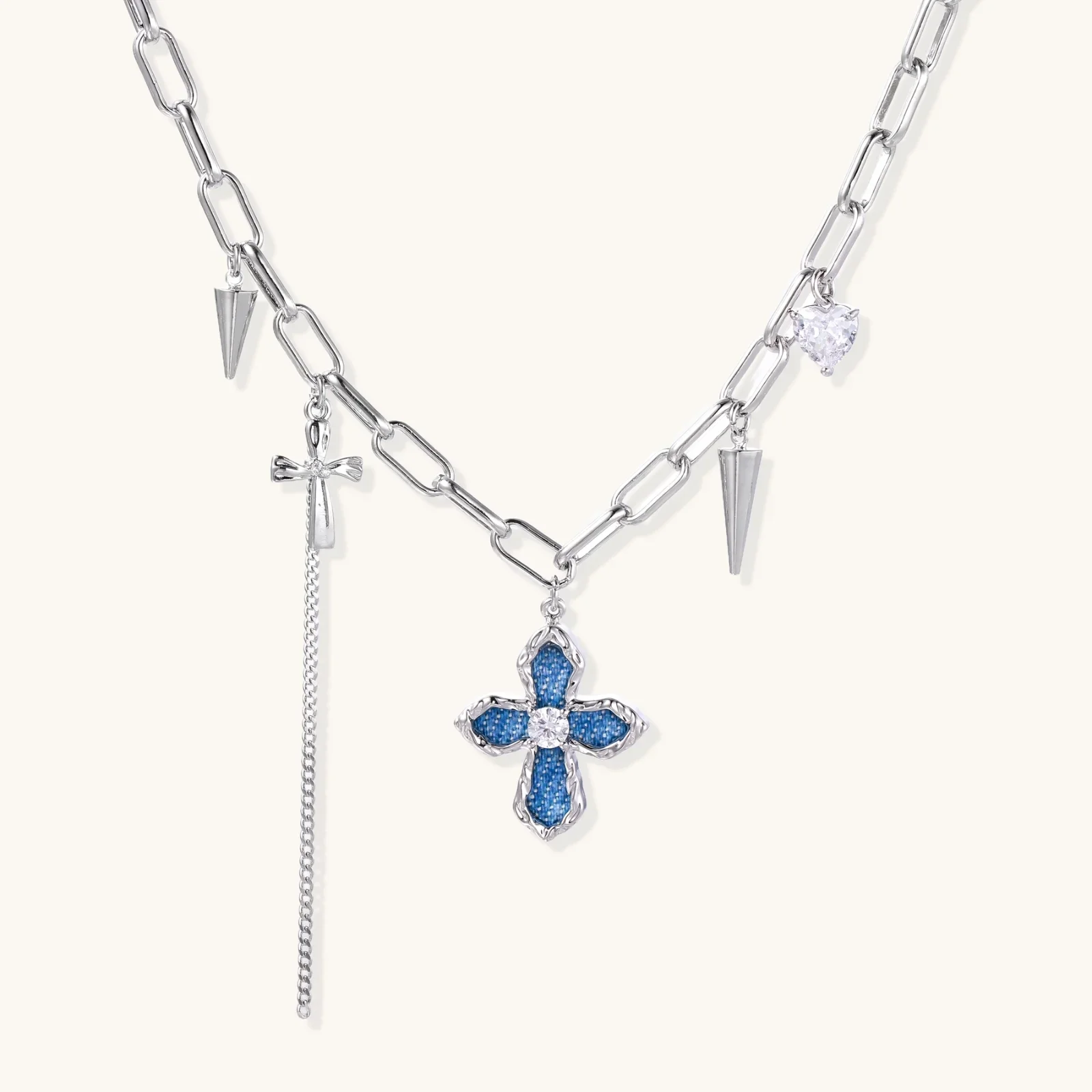 White gold plated chain necklace with blue textured cross pendant, spike charms, and mini cross detail on beige background