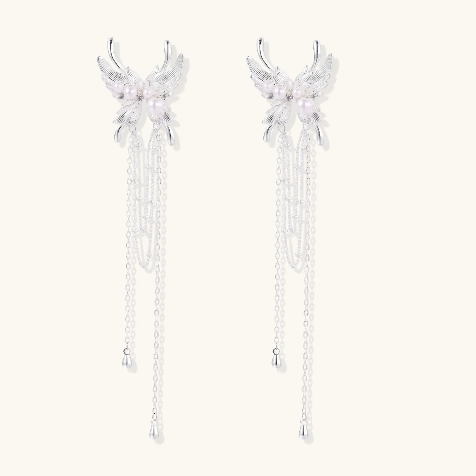 Elegant chandelier earrings with phoenix wing design, white pearls, and cascading silver chains on cream background