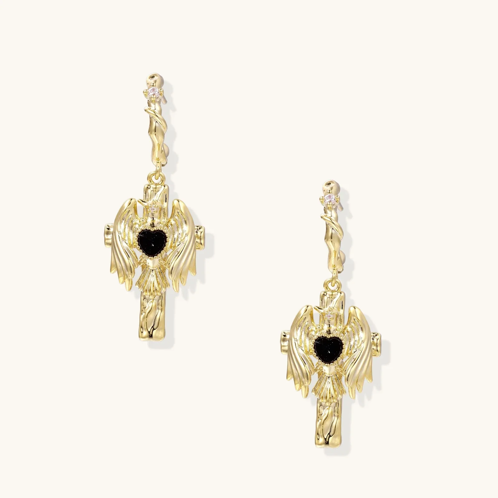 Gold angel wing drop earrings with black heart-shaped zirconia center and twisted posts on beige background