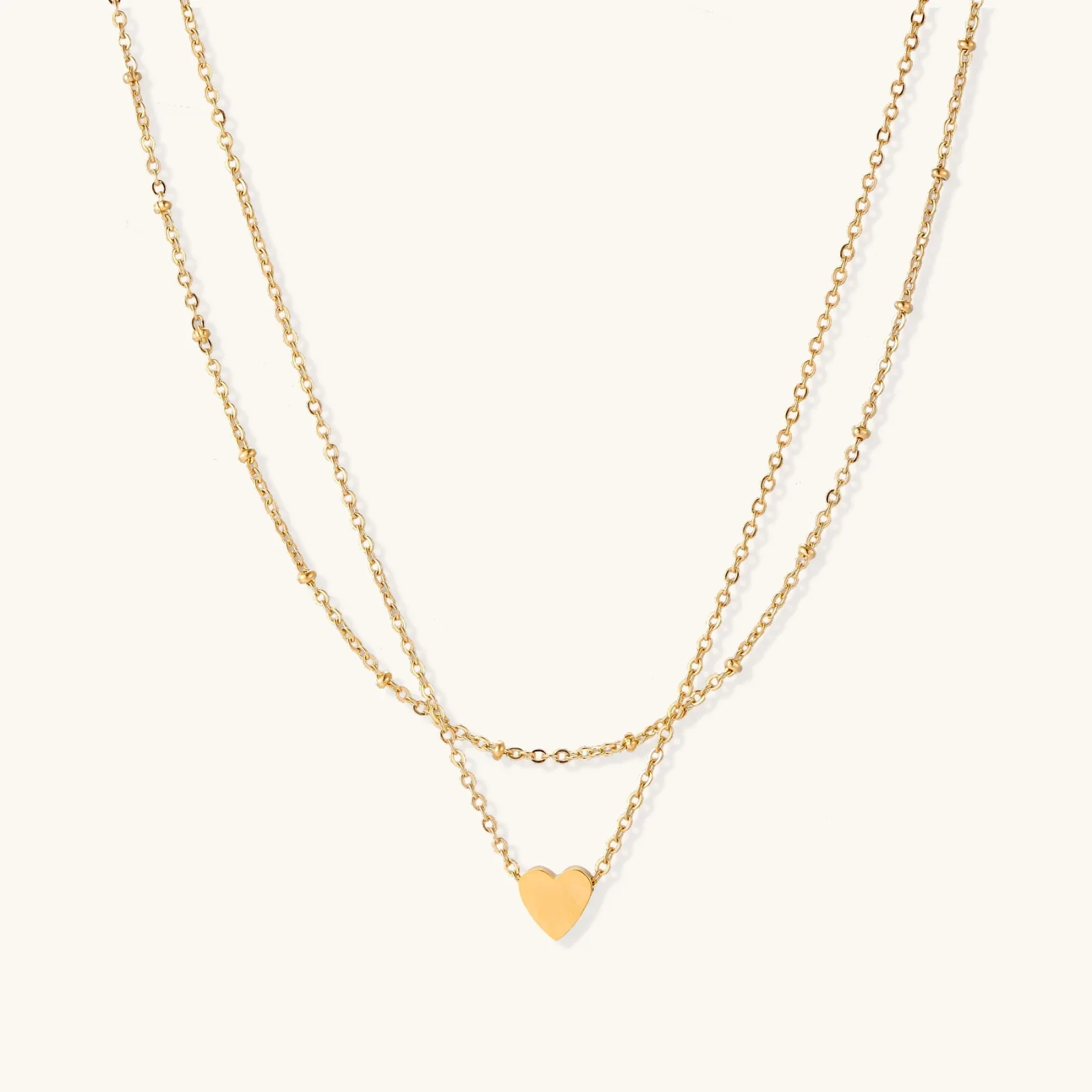 Delicate double-chain gold necklace with tiny heart pendant on cream background