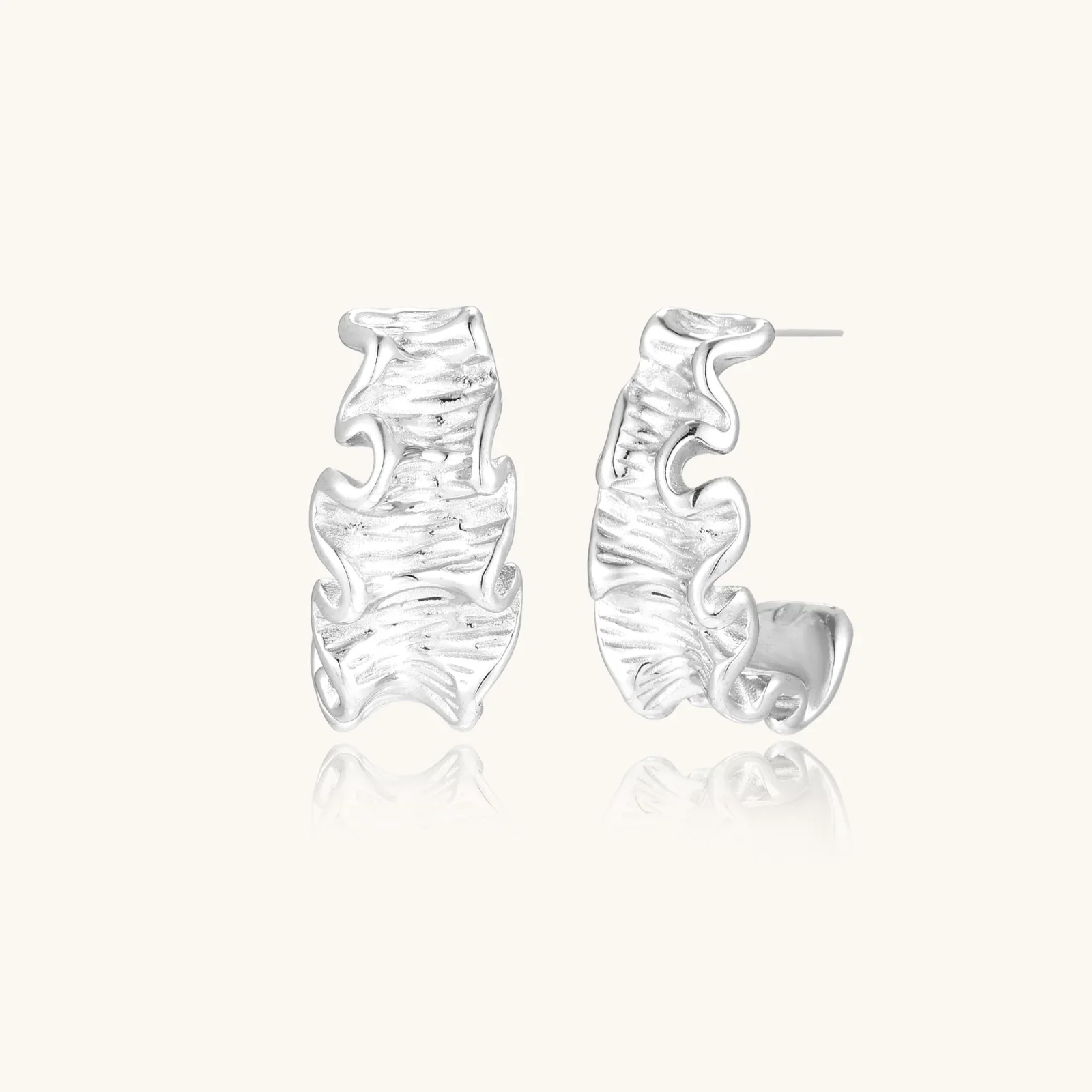 White gold plated sculptural hoop earrings with organic wavy edges and reflective metallic finish on cream background