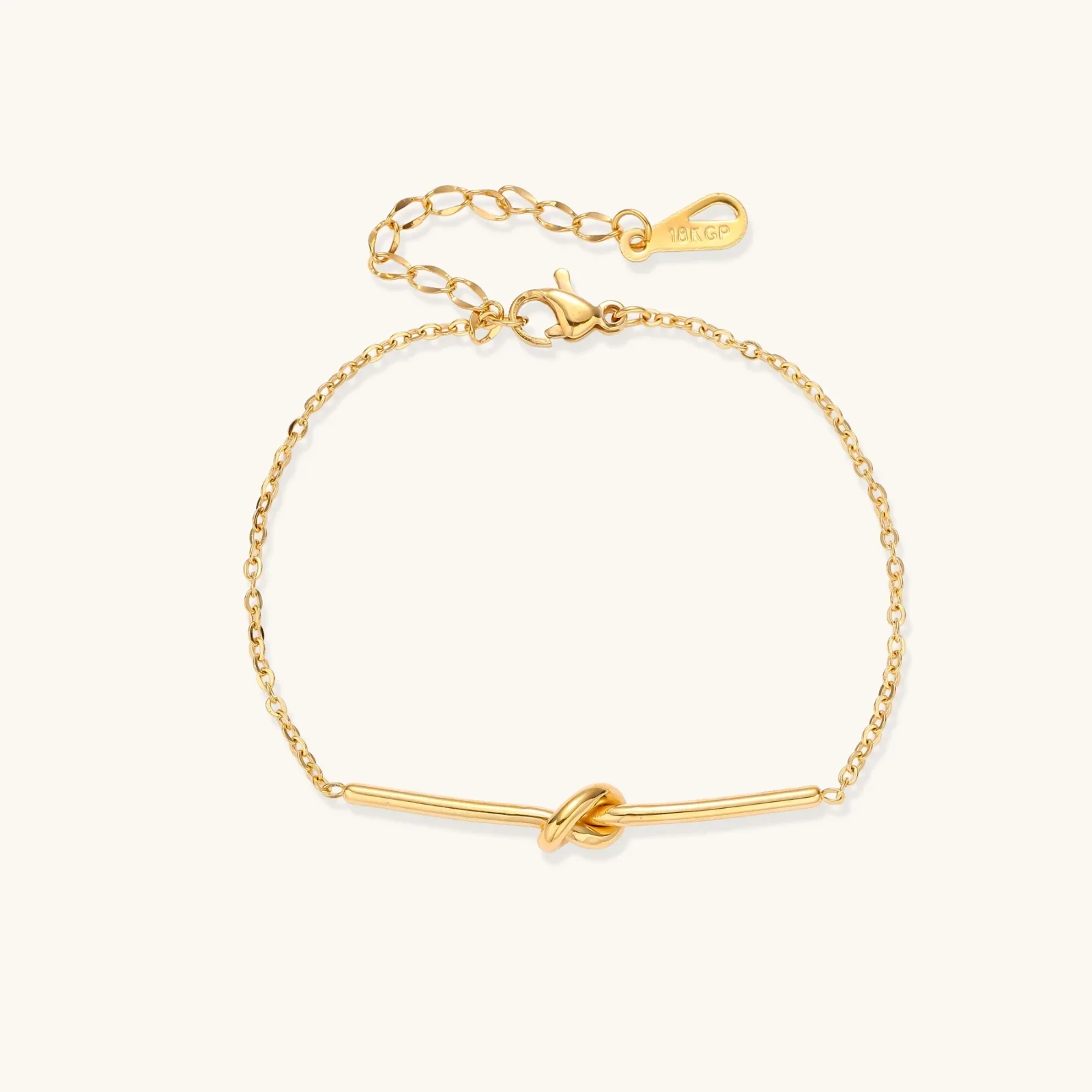 Delicate gold chain bracelet with minimalist bar and centered knot detail on cream background