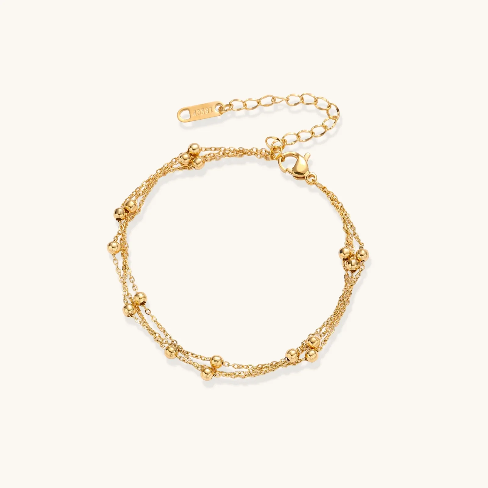 Three-strand gold-plated bracelet with clustered ball beads and adjustable clasp on cream background