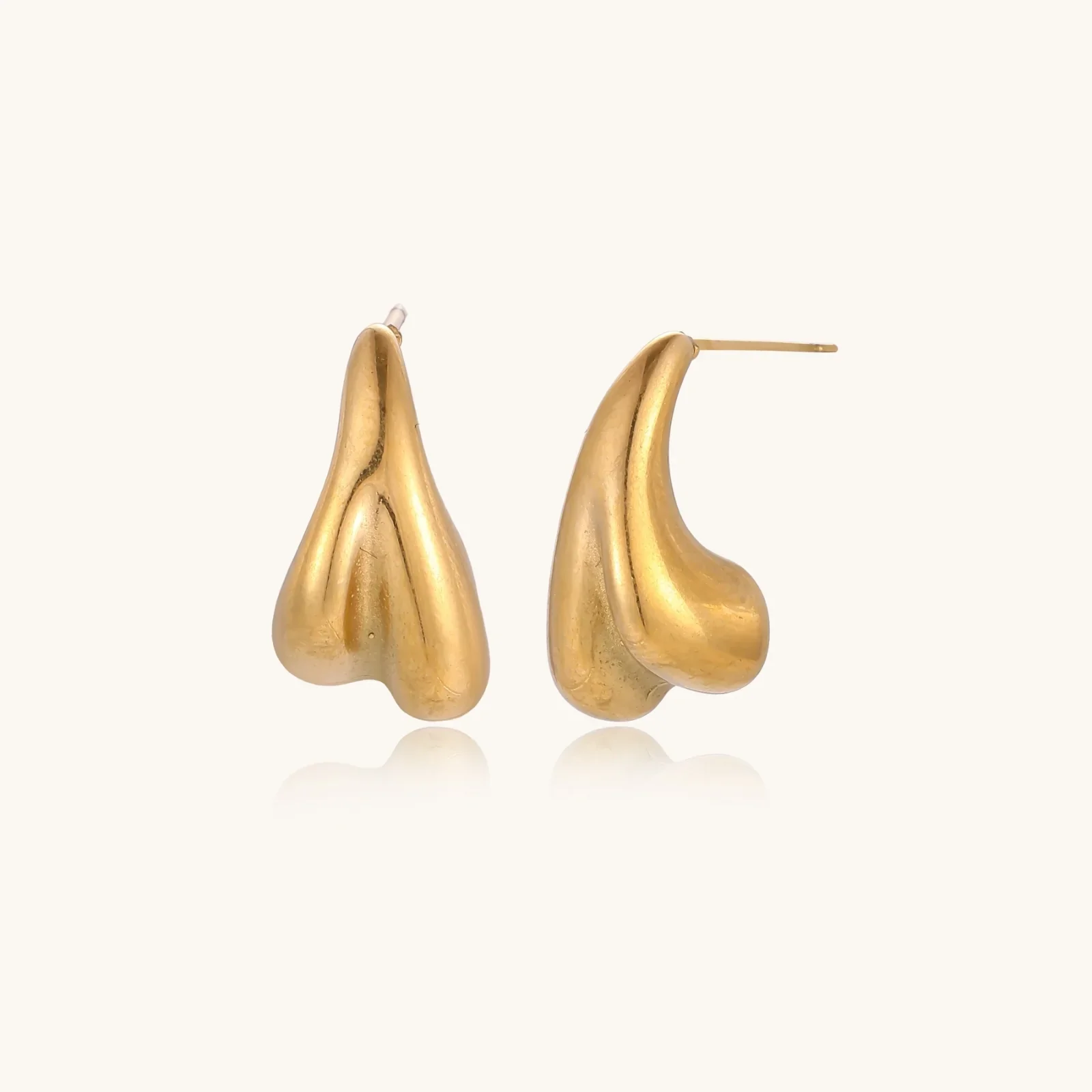 Pair of sculptural gold stud earrings with twisted organic forms on cream background