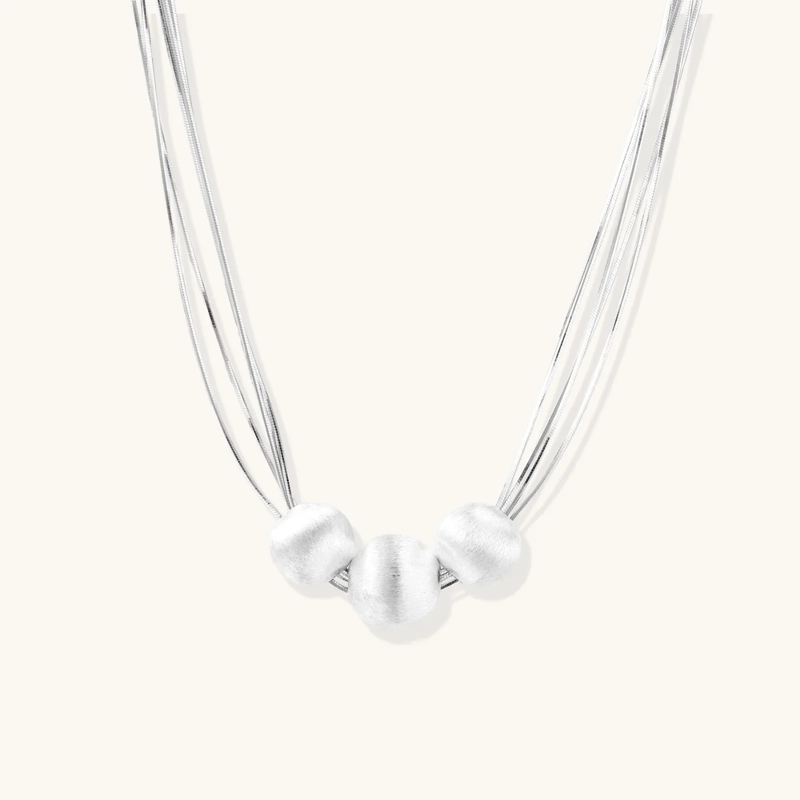 Sterling silver multi-strand necklace with three brushed round beads on cream background