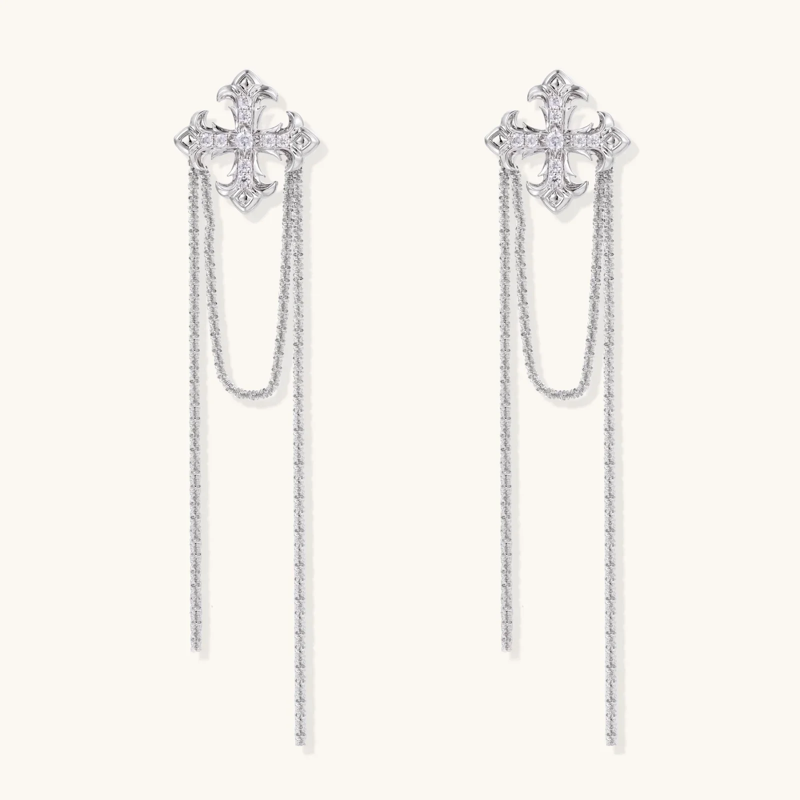 White gold plated baroque cross stud earrings with long cascading zirconia chains on cream background
