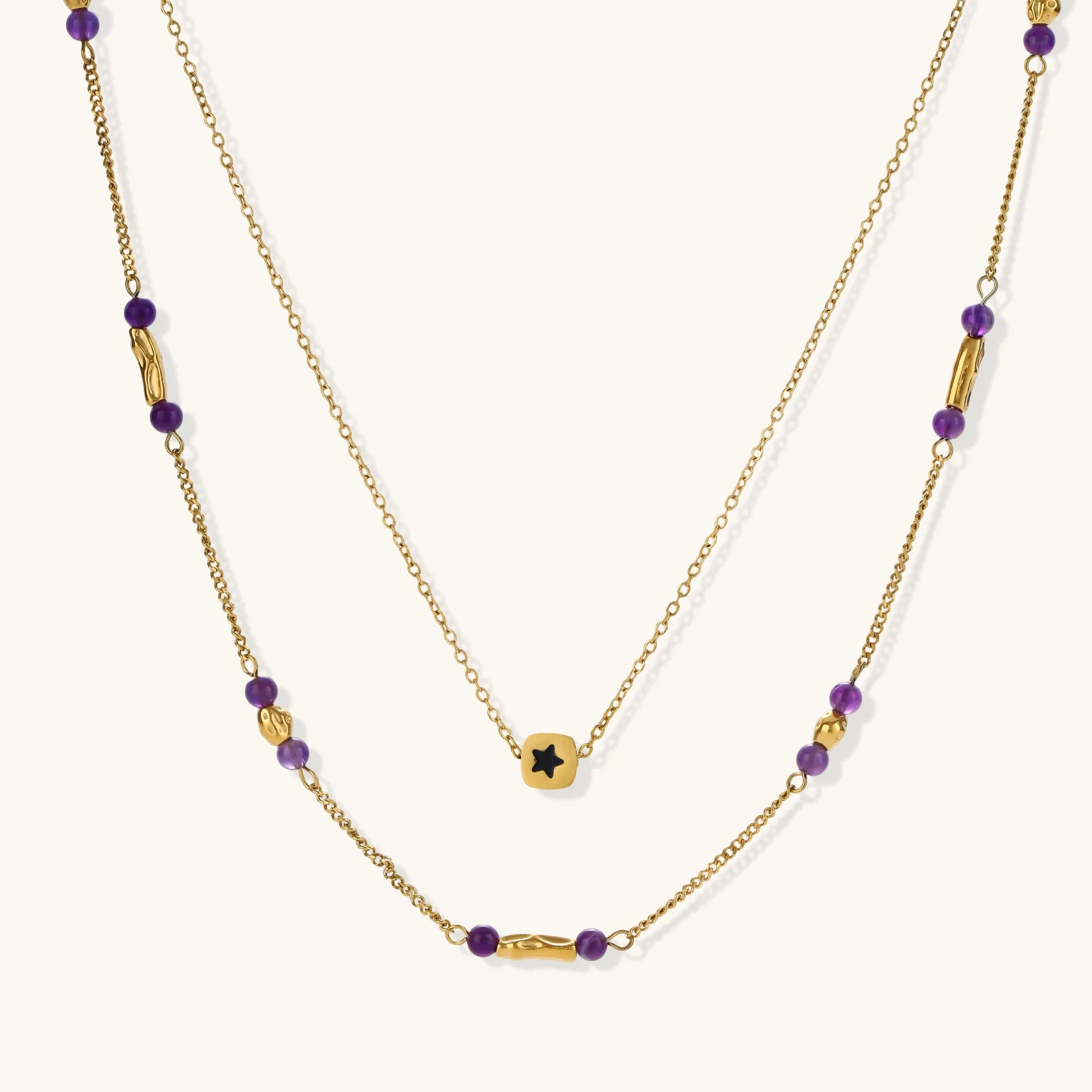 Two layered gold-tone necklaces with purple stone beads and star pendant against cream background.