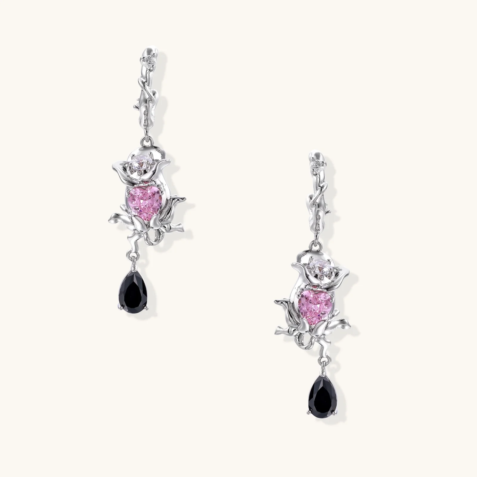 Silver-toned drop earrings with ornate rose design, pink zirconia center, and black teardrop stones on cream background