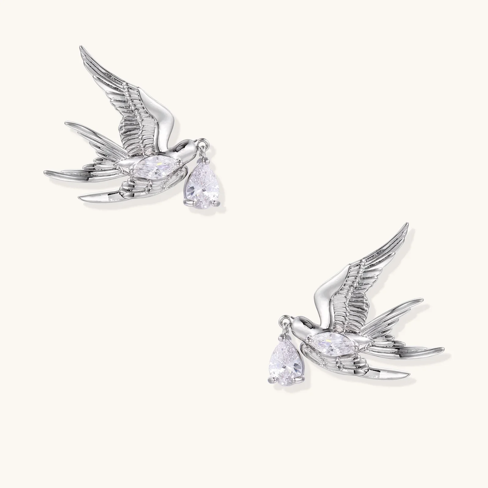 Silver-toned swallow stud earrings with detailed wings carrying teardrop zirconia crystals on white background