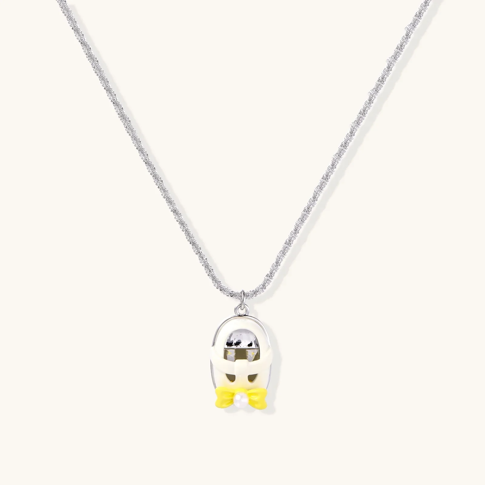 Chrome egg-shaped pendant with kawaii face, yellow bow, and pearl detail on silver chain against white background