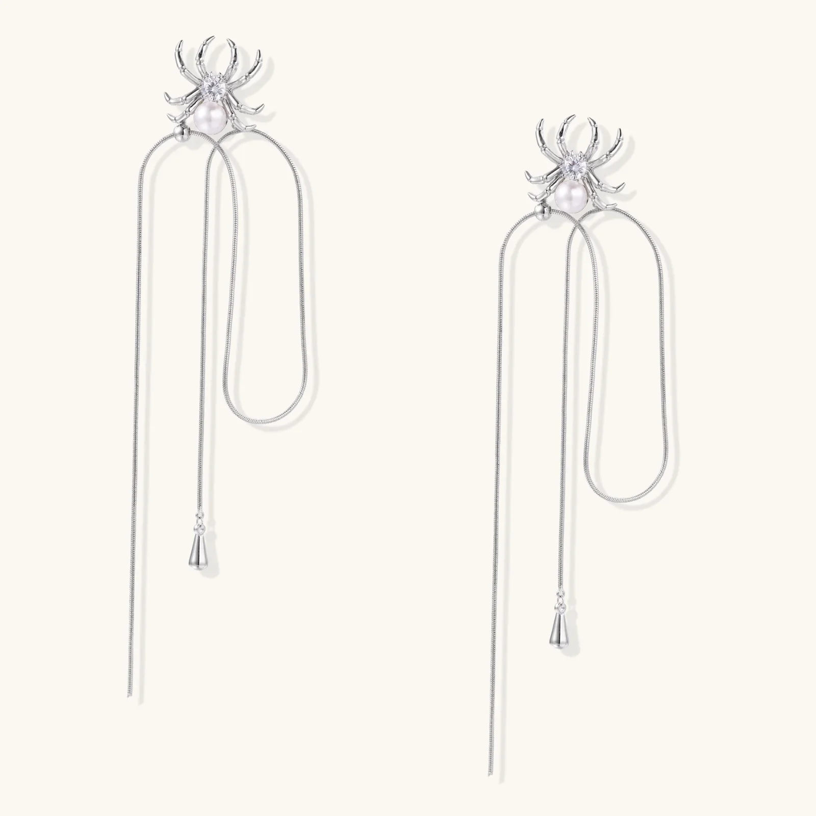 White gold plated spider earrings with pearl body and long threader chains on beige background