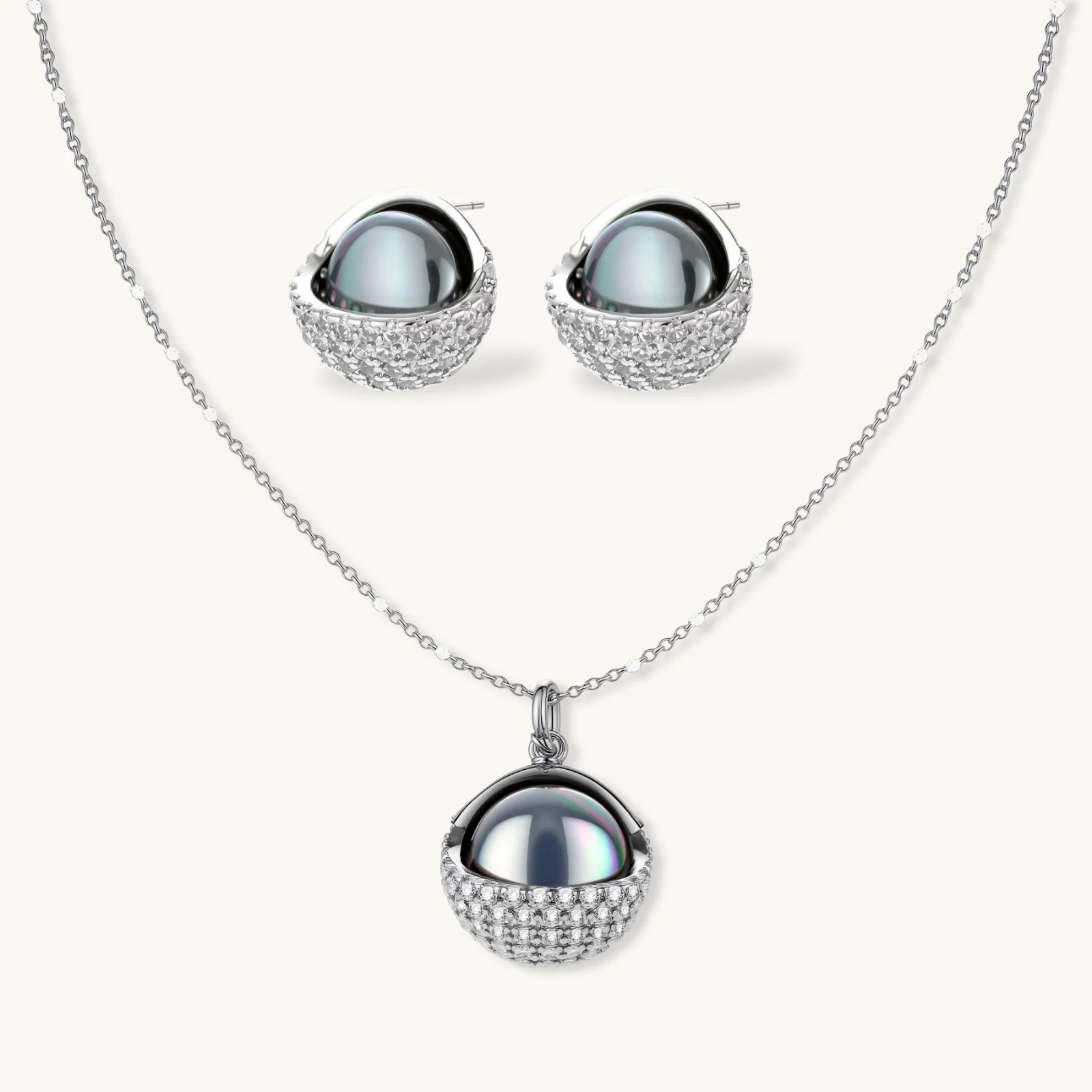 Elegant spherical pendant necklace and earrings set featuring crystal-pavé bottom half in gold or silver finish on white background.